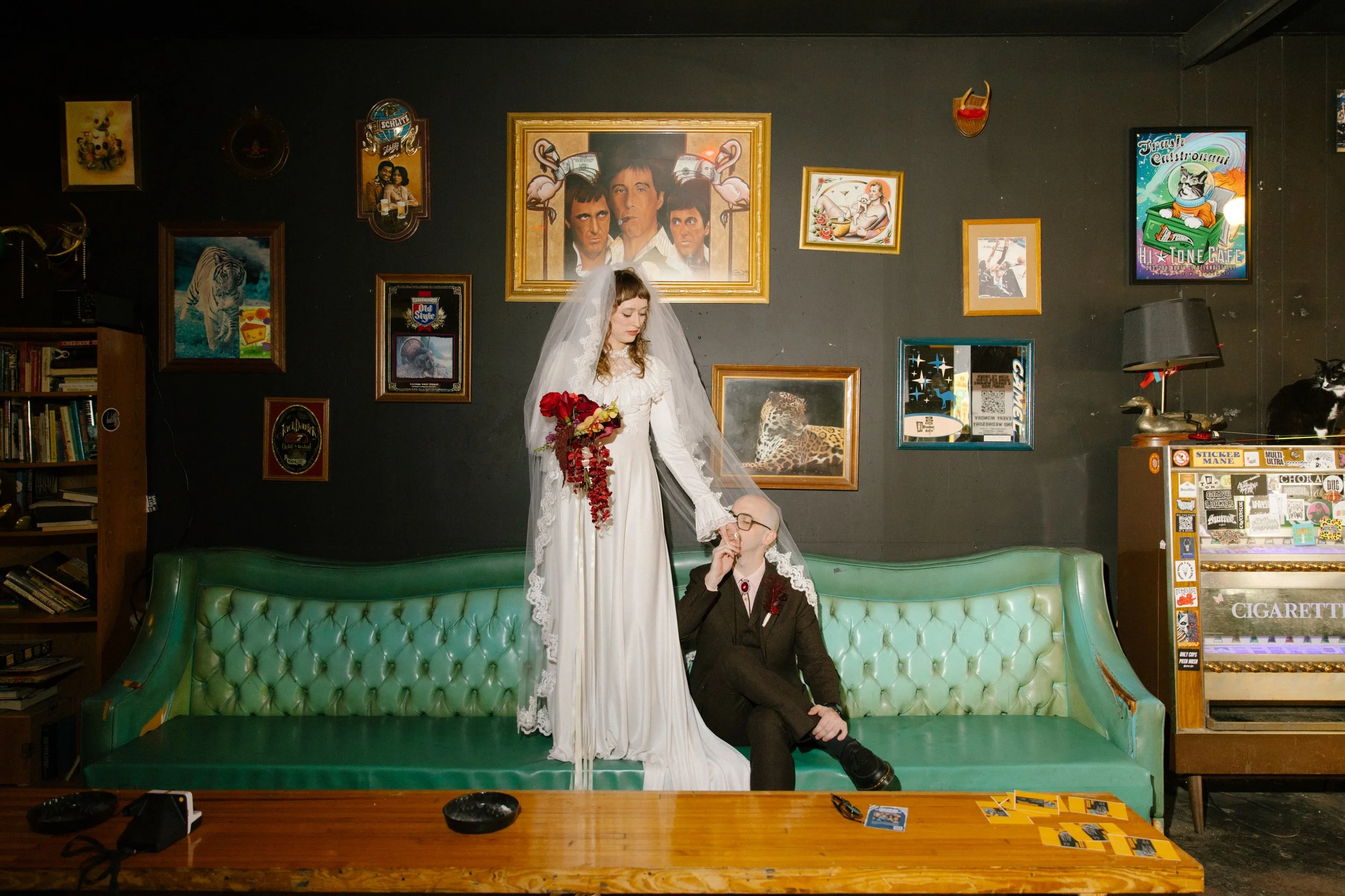 Bride standing on a green couch while groom sits beside her in a vintage bar setting, reflecting bold and expressive unique wedding ideas