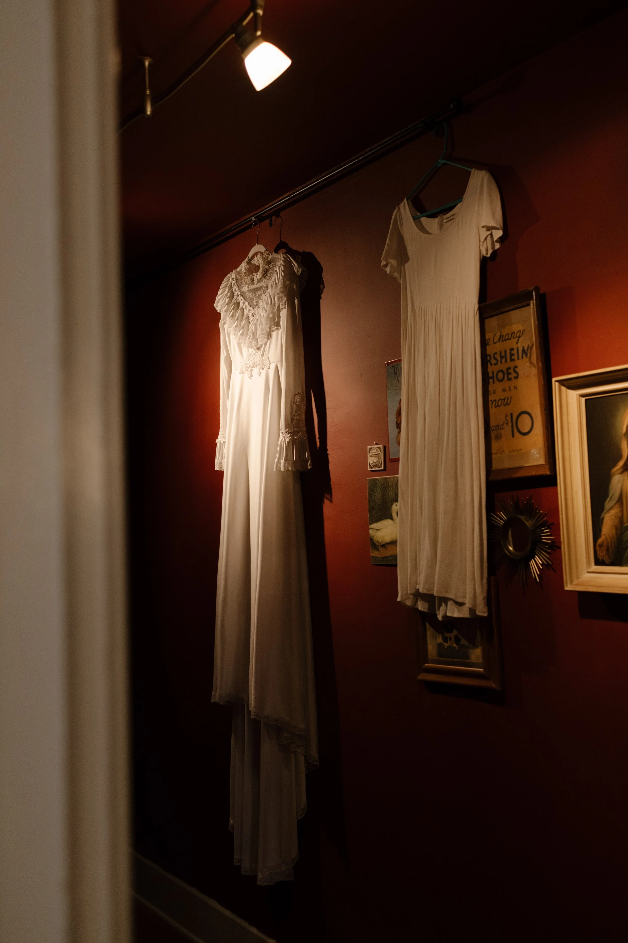 Wedding dresses hanging on a red wall in a dimly lit room, adding moody and artistic texture to unique wedding ideas