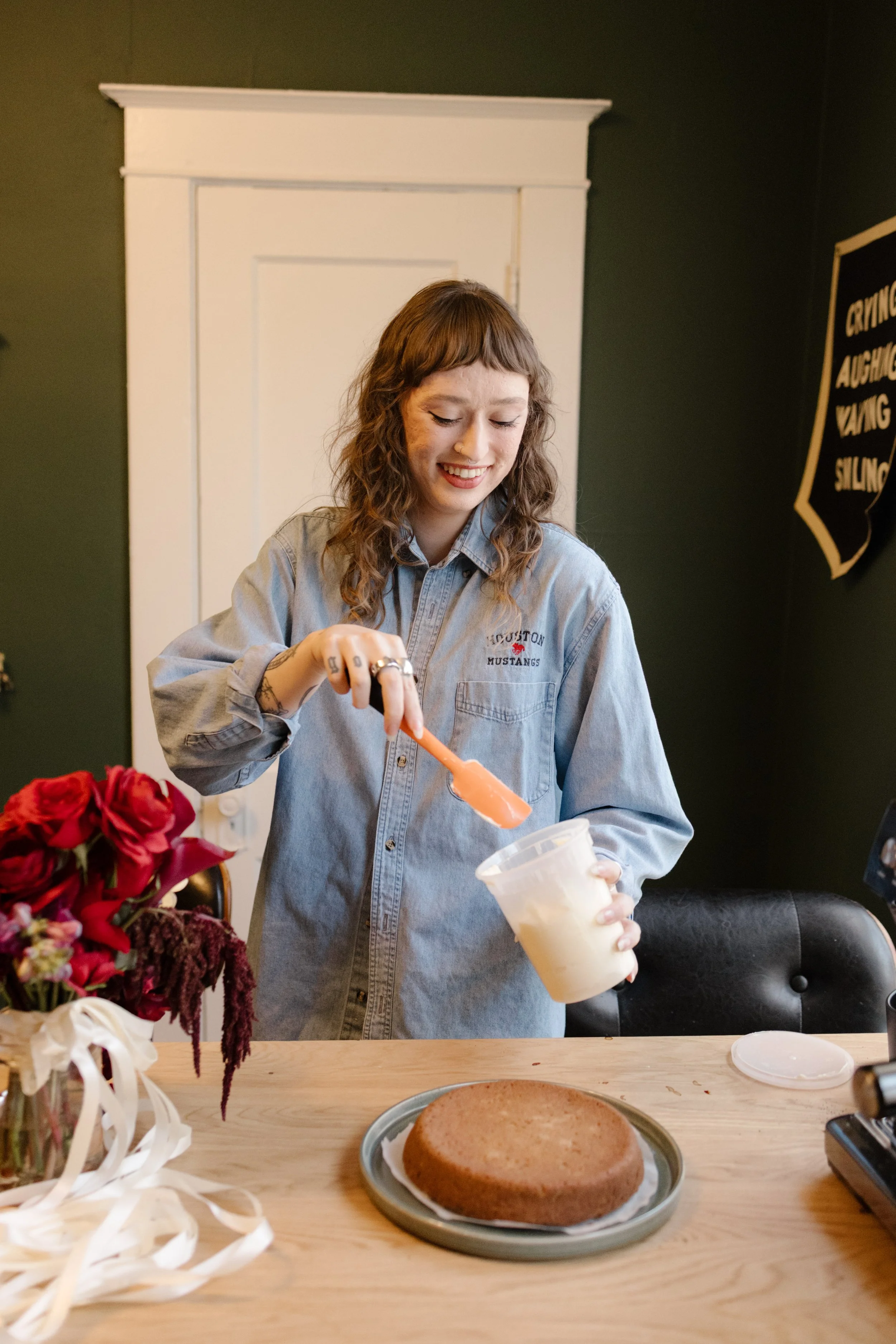 Bride smiling while frosting a cake in her kitchen before the wedding, highlighting relaxed and personal unique wedding ideas