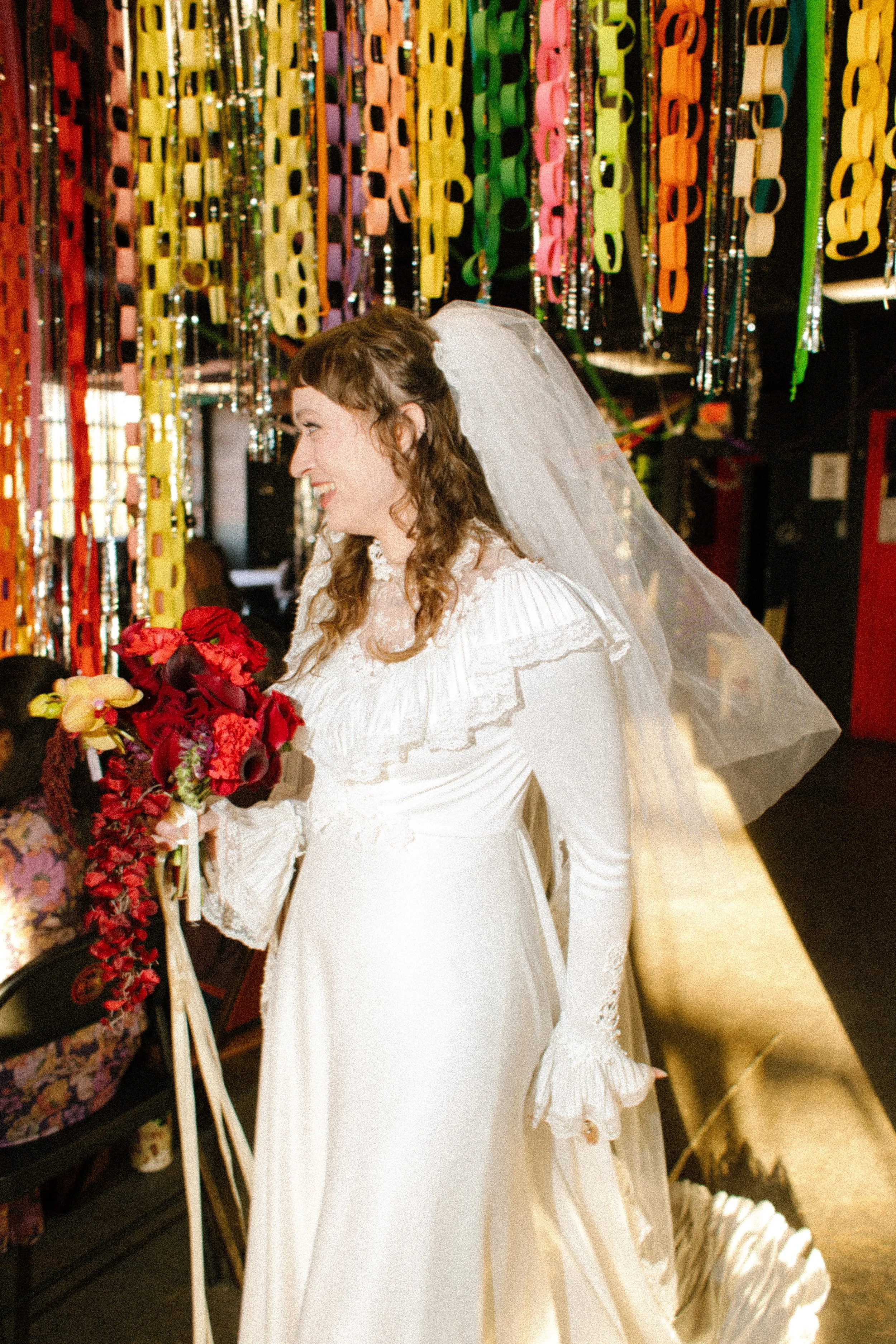 Bride holding a bouquet while walking through decorated venue space filled with hanging paper chains and lights