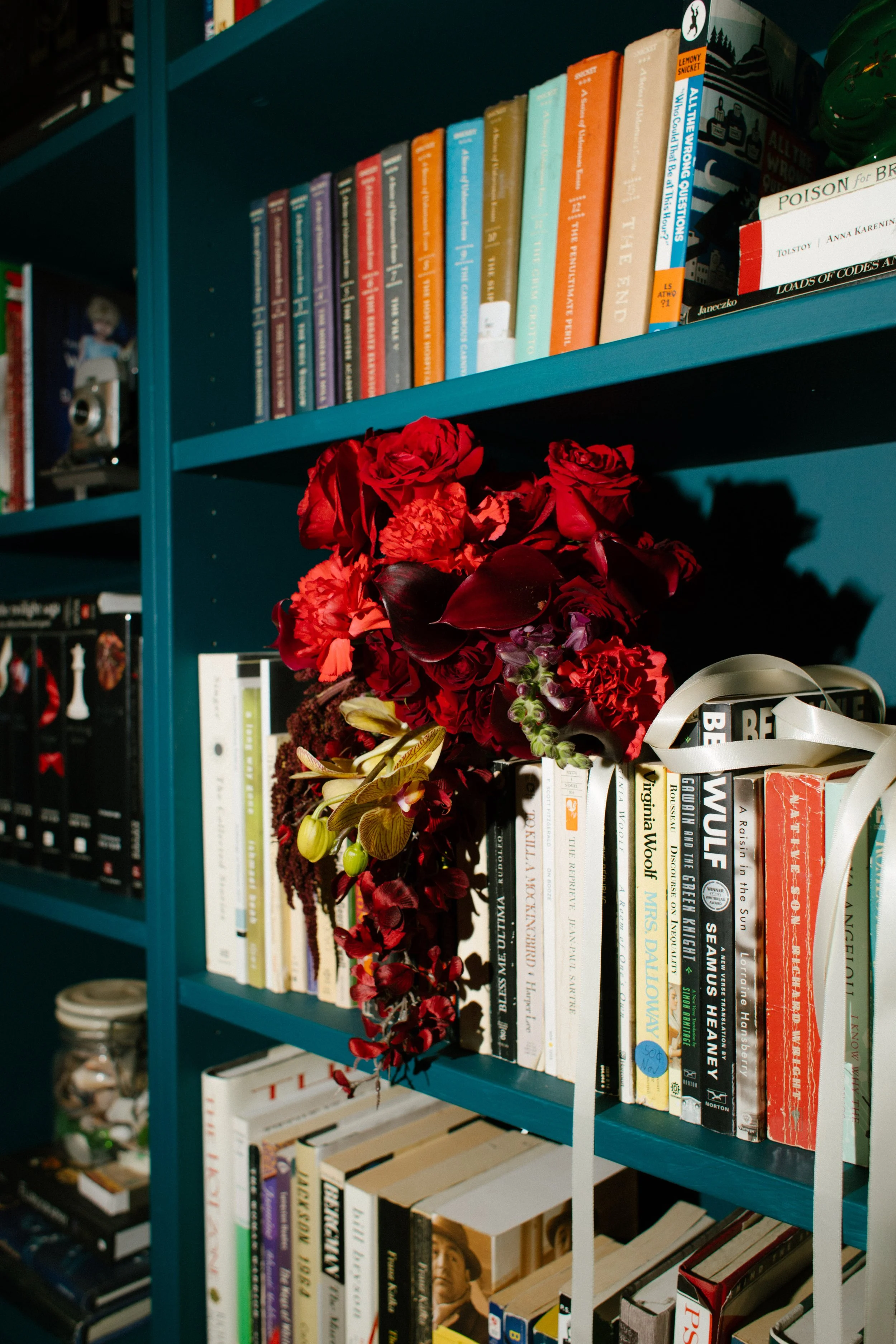 Red wedding bouquet placed on a bookshelf with colorful books, showcasing artistic and layered unique wedding ideas