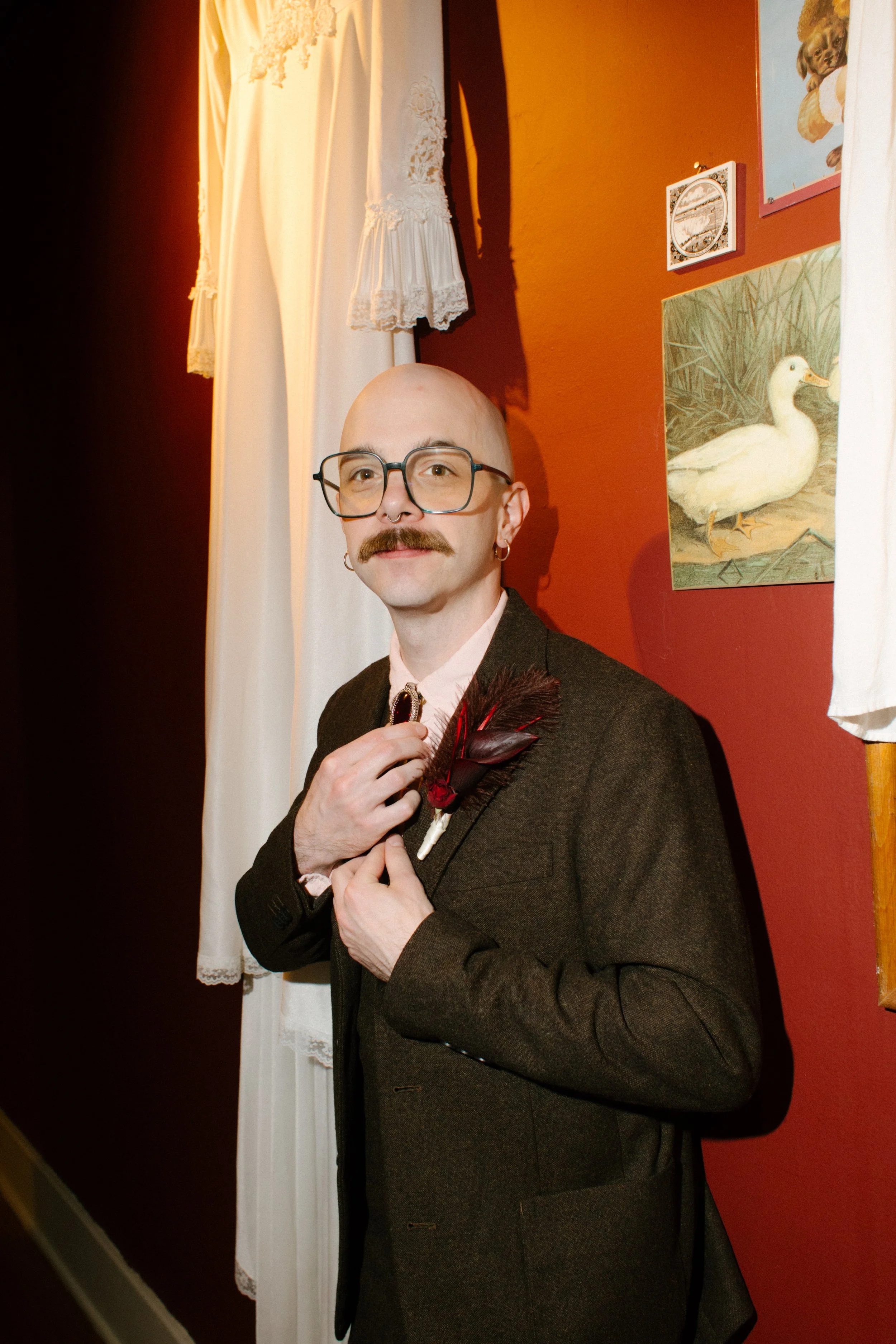 Groom adjusting his tie in a red room with vintage decor, capturing stylish and personality-driven wedding details
