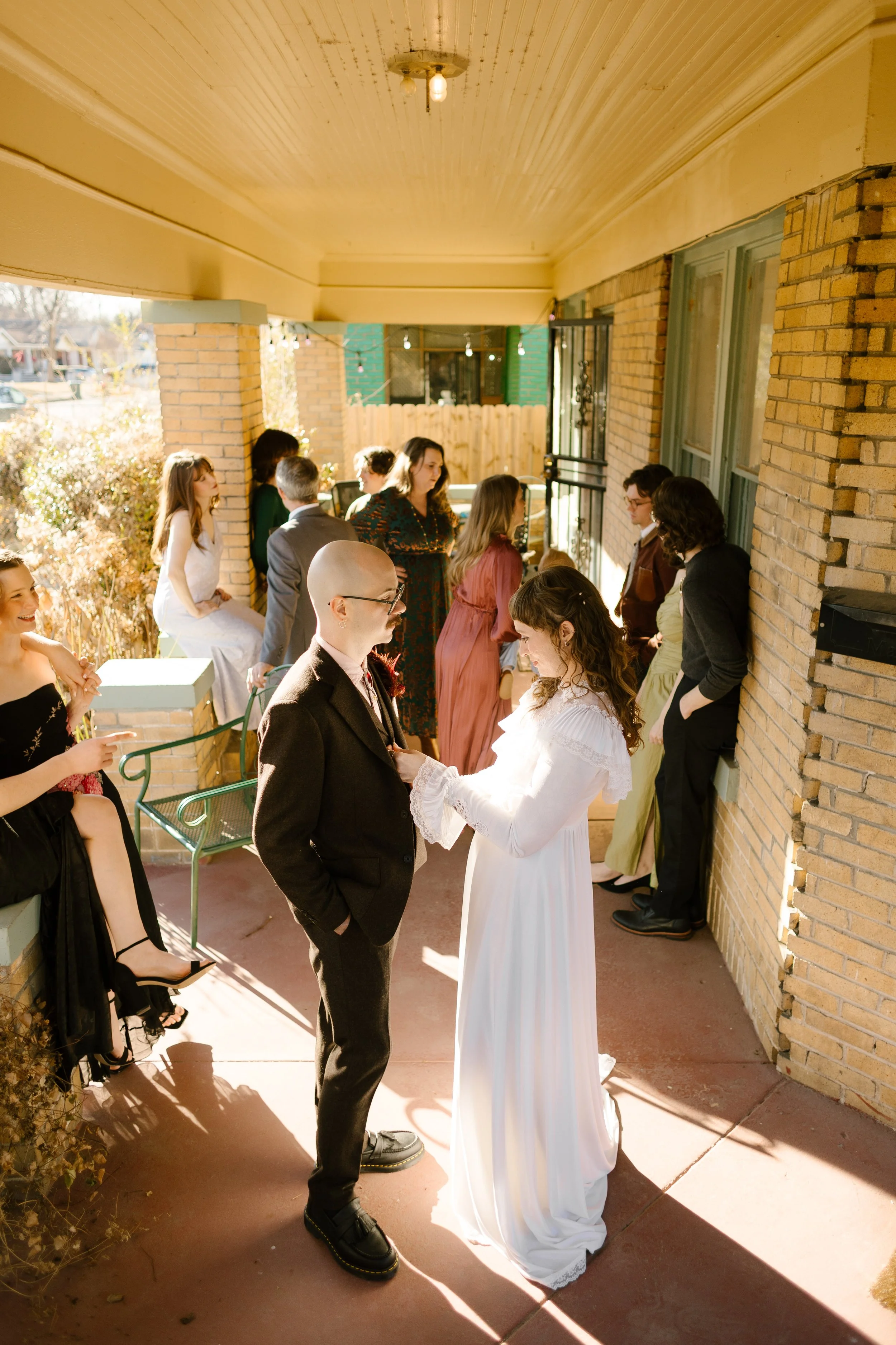 Bride and groom standing together on a front porch surrounded by friends, capturing a relaxed and community-centered wedding moment