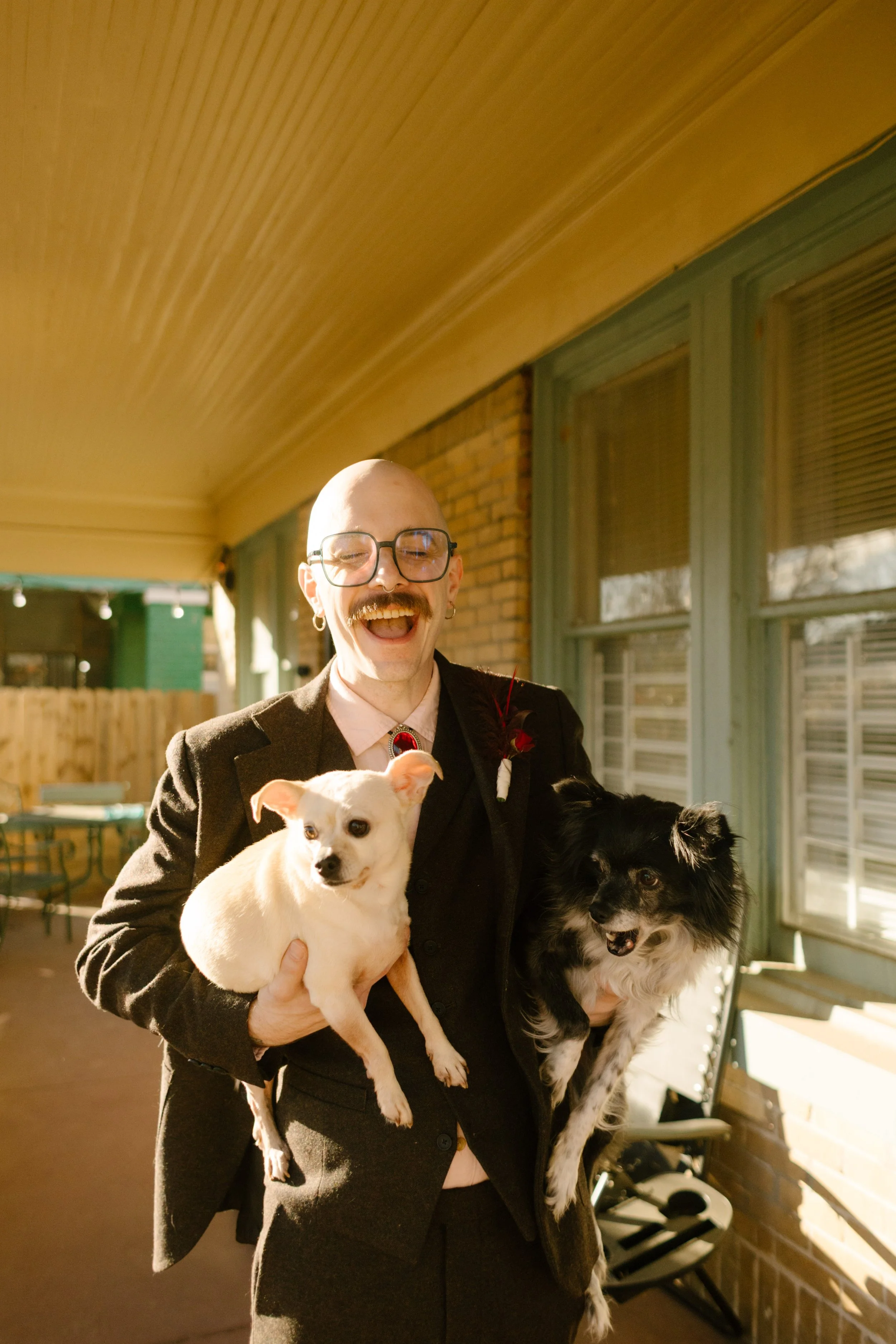 Groom holding two dogs on a sunny porch during wedding morning, adding playful and personality-driven unique wedding ideas