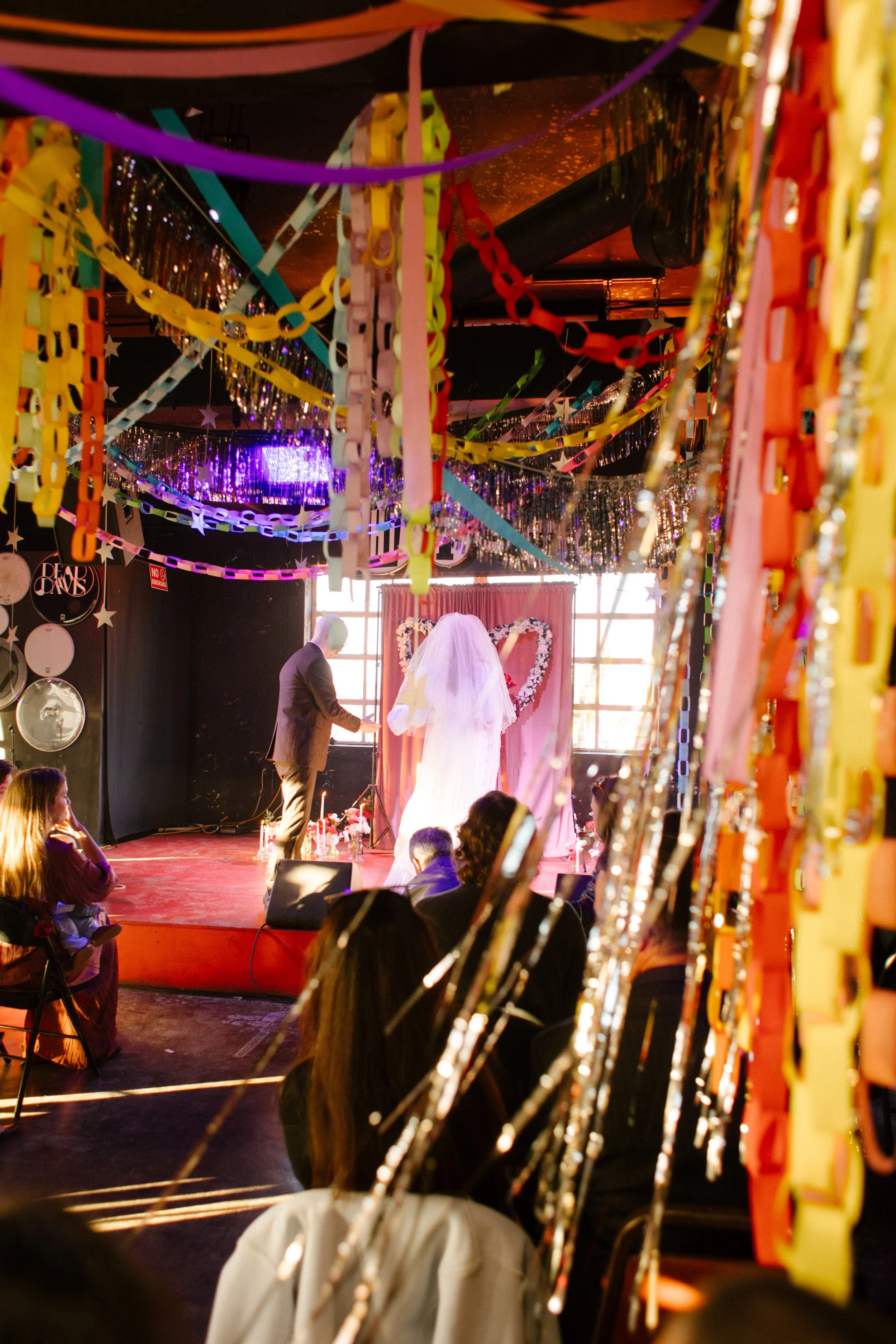 Wide view of wedding ceremony with colorful paper chains and streamers hanging from ceiling, showcasing bold and creative unique wedding ideas