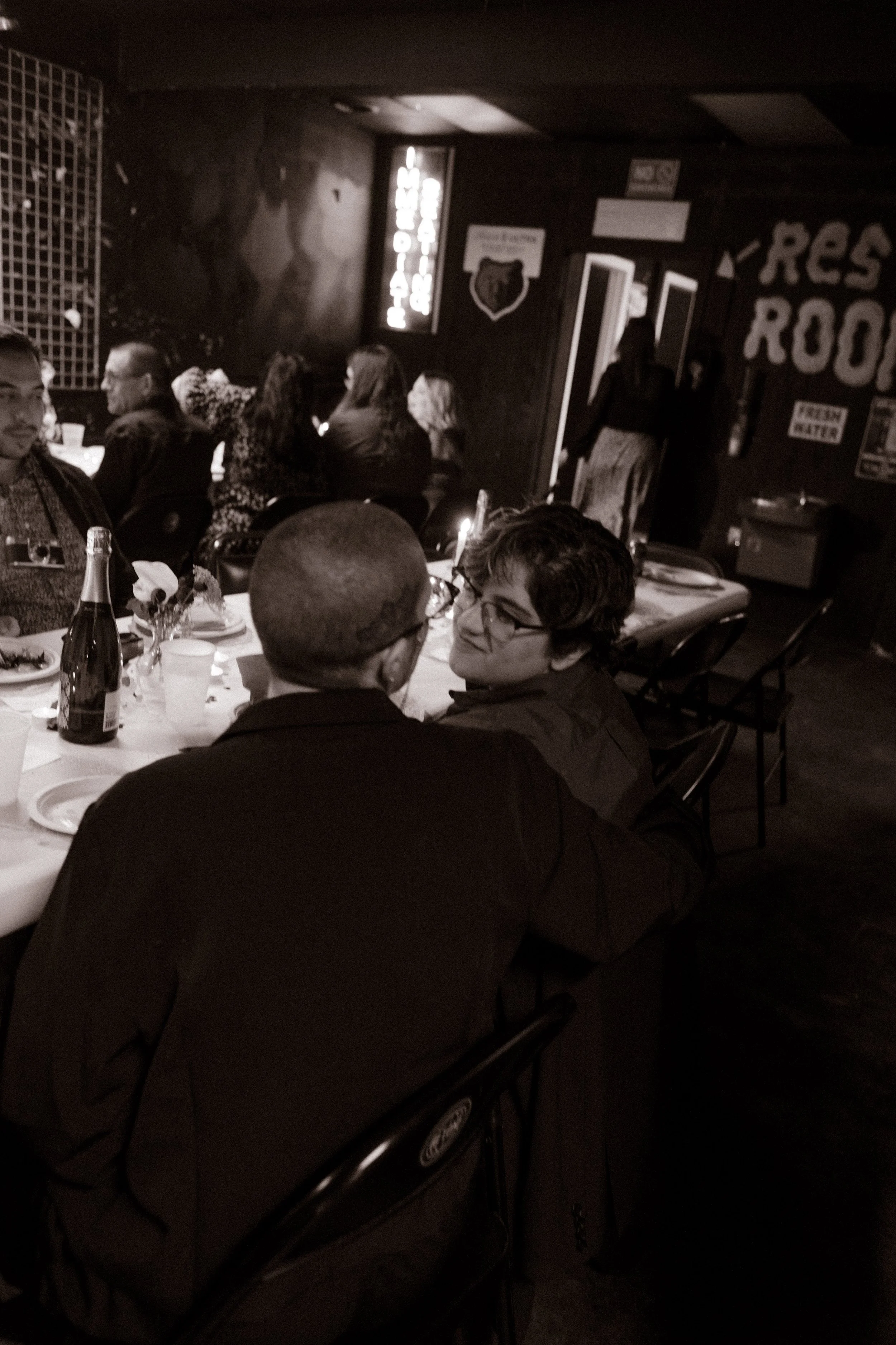 Black and white candid photo of couple sitting together at reception table, capturing quiet and intimate connection