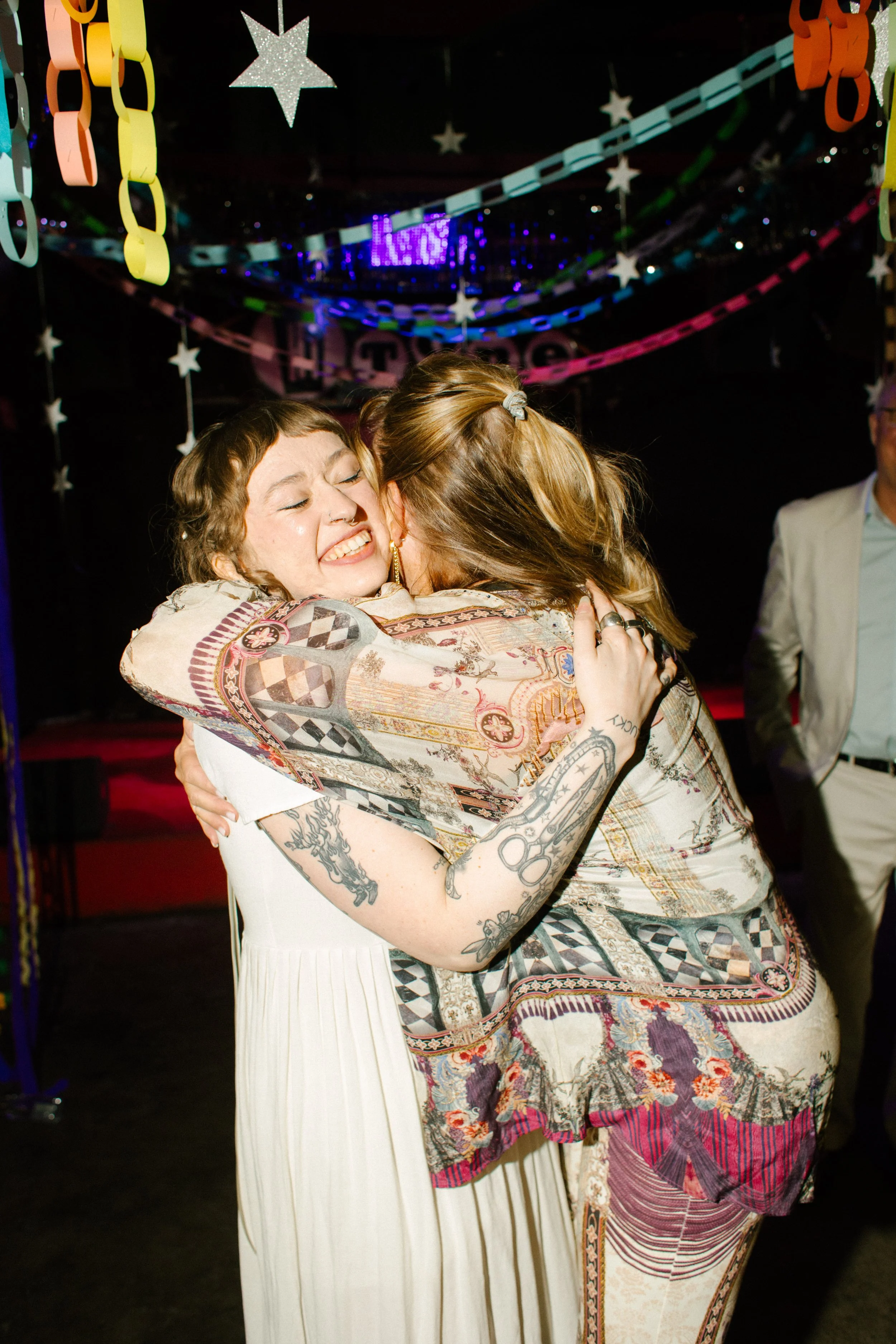 Bride hugging guest tightly under colorful paper chain decorations, capturing emotional and community-centered wedding moment