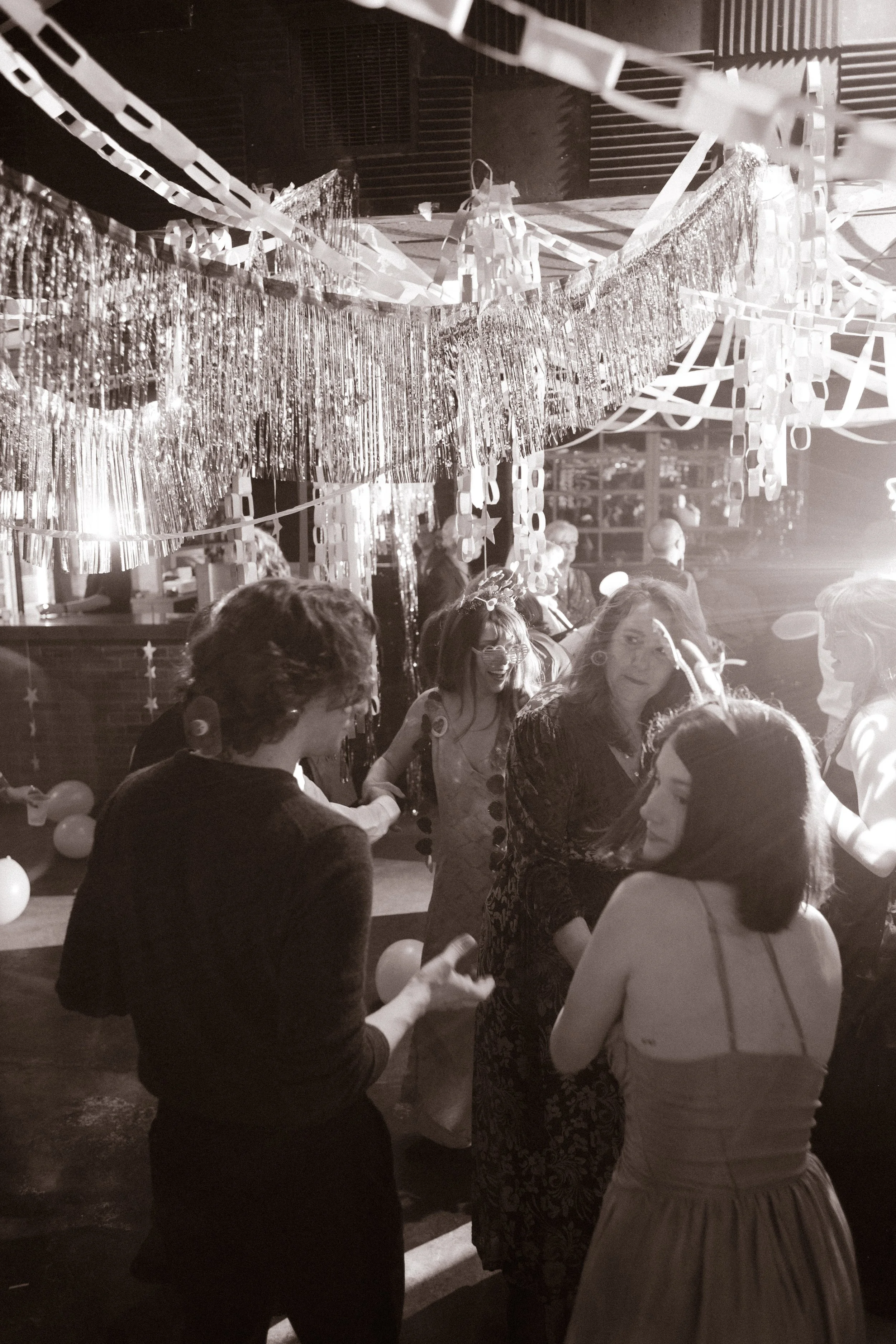 Black and white photo of guests dancing under streamers and tinsel, highlighting lively and unconventional wedding reception energy