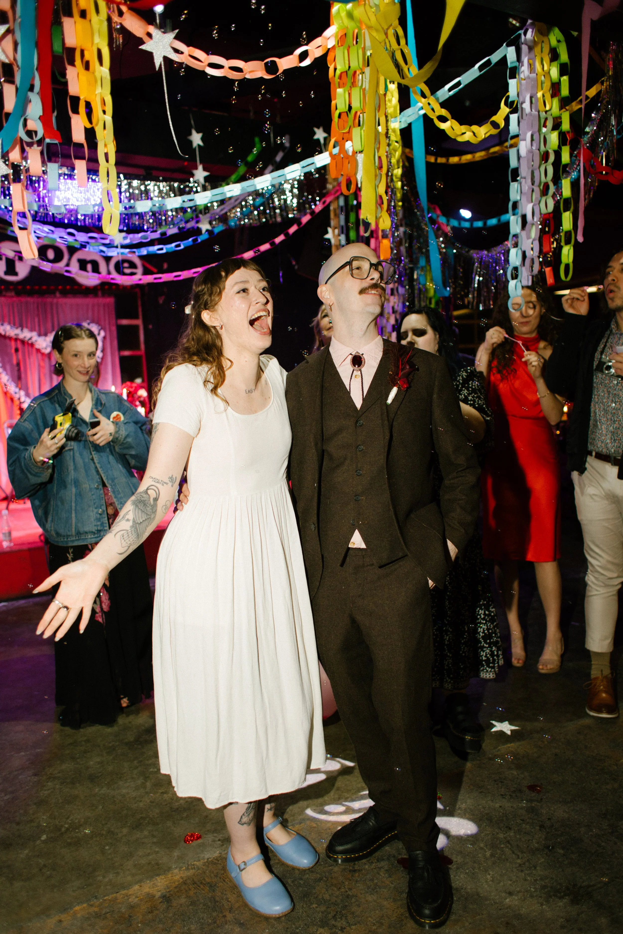Bride and groom reacting joyfully during reception surrounded by guests and colorful decor, capturing expressive and personality-driven unique wedding ideas