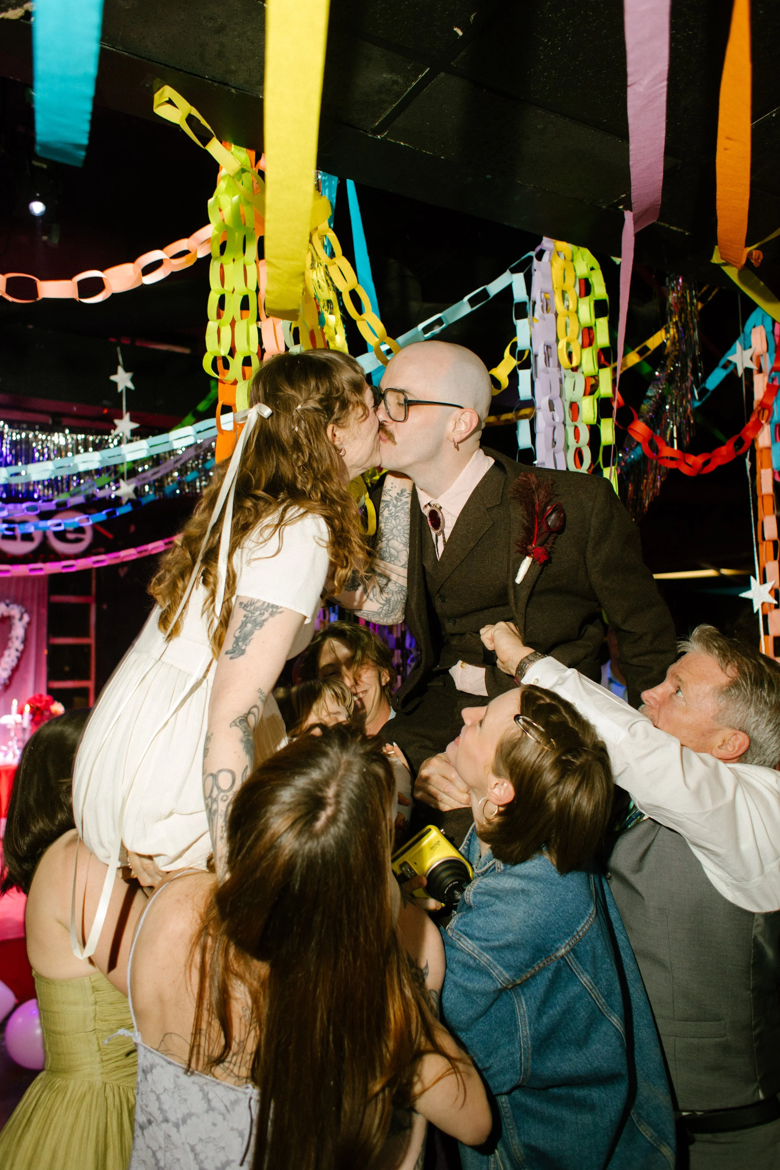 Bride and groom lifted by guests while kissing under colorful decorations, showcasing energetic and unforgettable unique wedding ideas