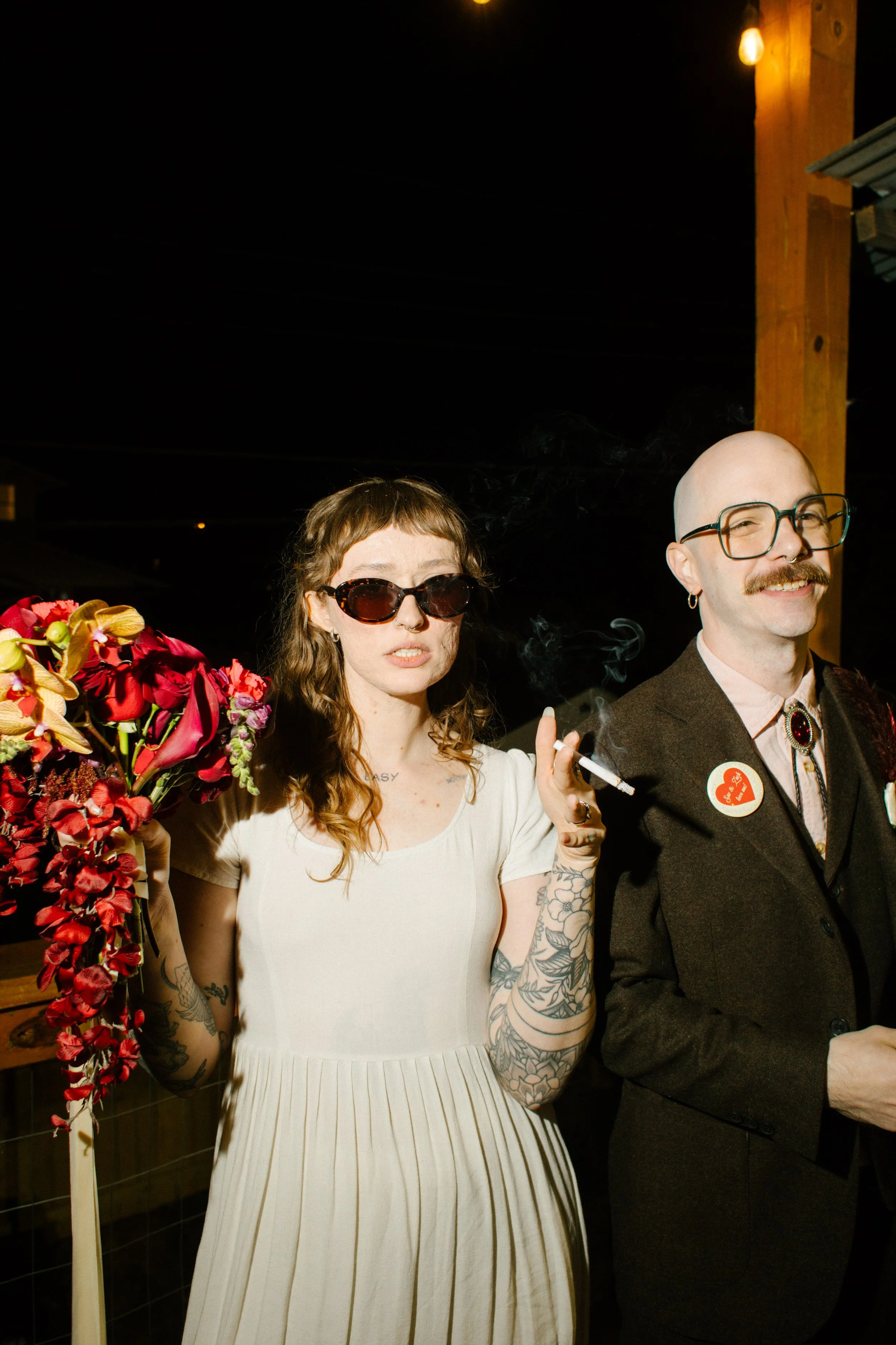 Bride and groom standing together at night holding drinks and bouquet, capturing candid and personality-filled unique wedding ideas