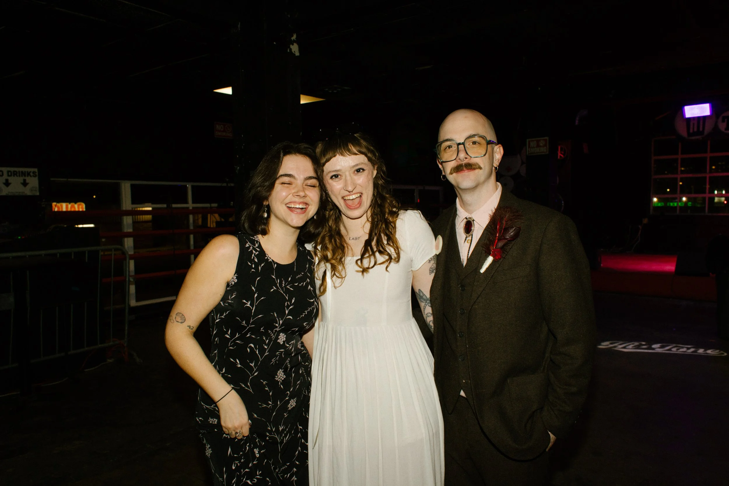 Bride and groom posing with friend during reception, capturing joyful and community-centered wedding moments