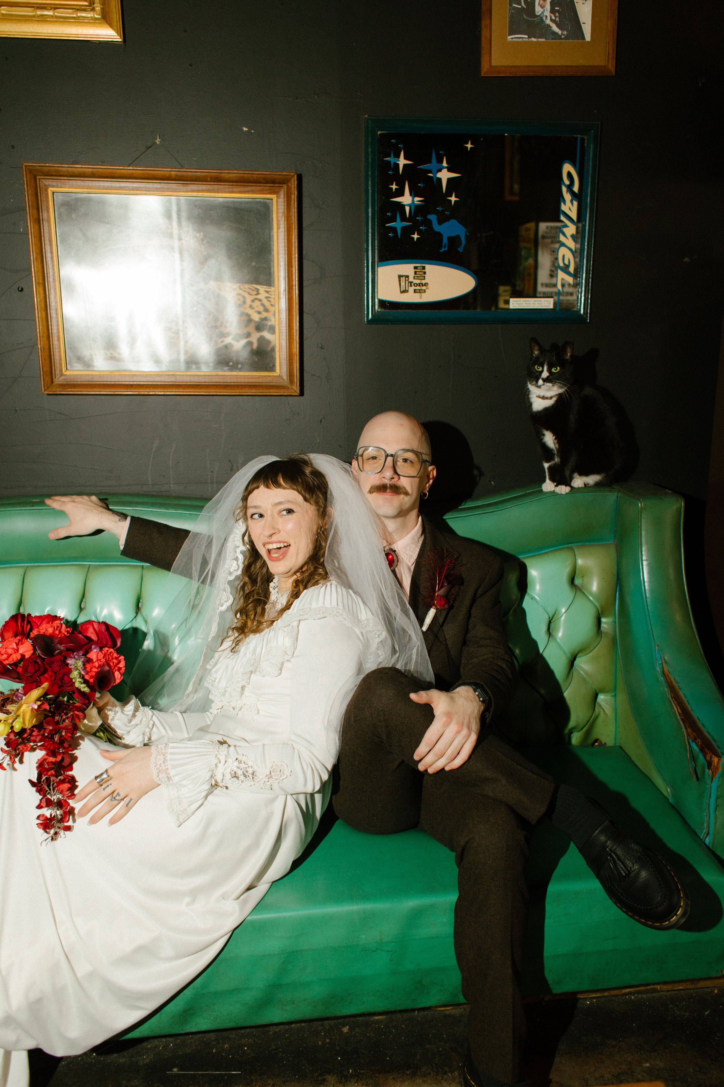 Bride and groom lounging on green couch with cat beside them, showcasing quirky and memorable unique wedding ideas