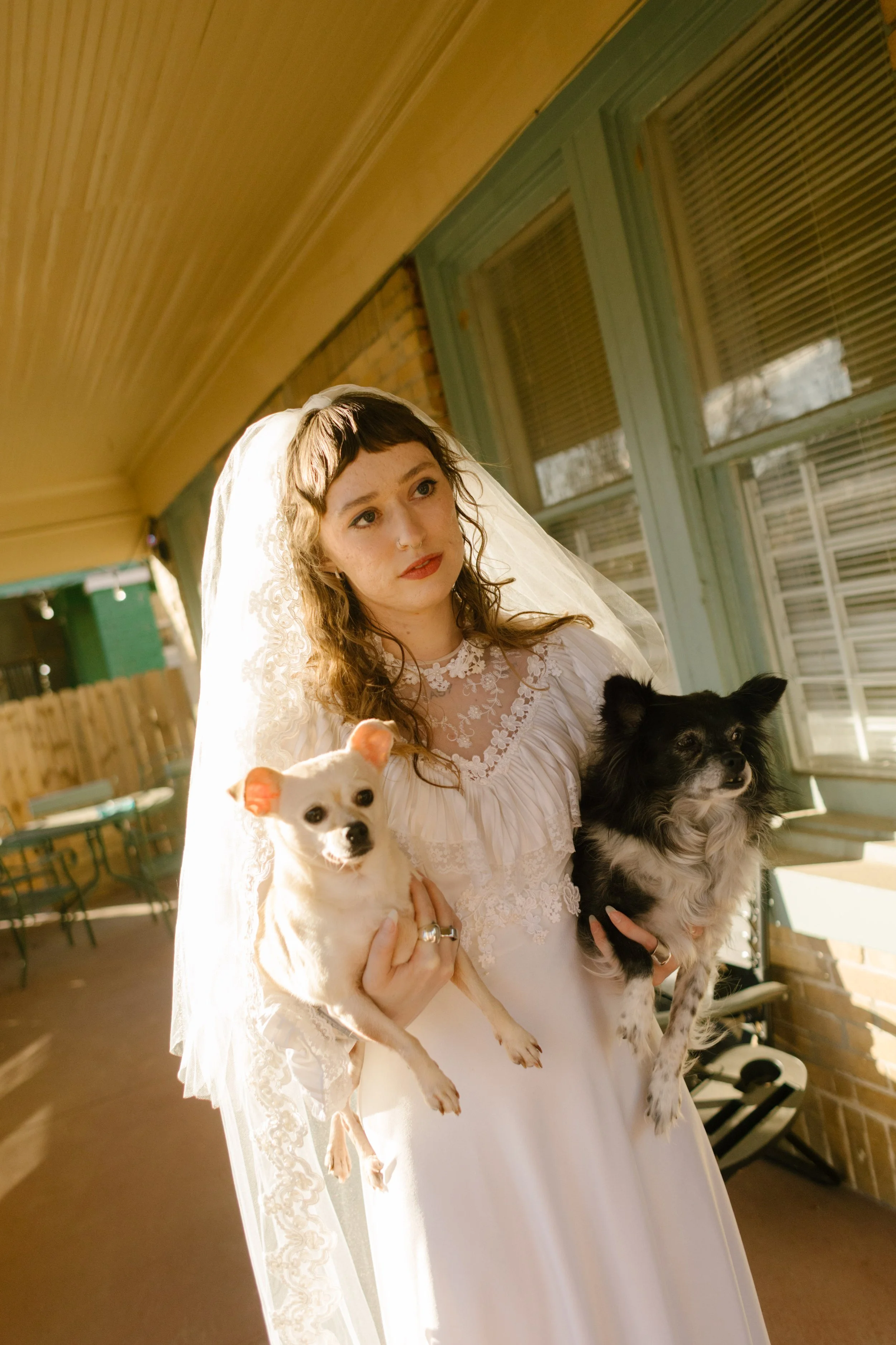 Bride holding two small dogs on porch in wedding dress, highlighting personal and pet-friendly unique wedding ideas