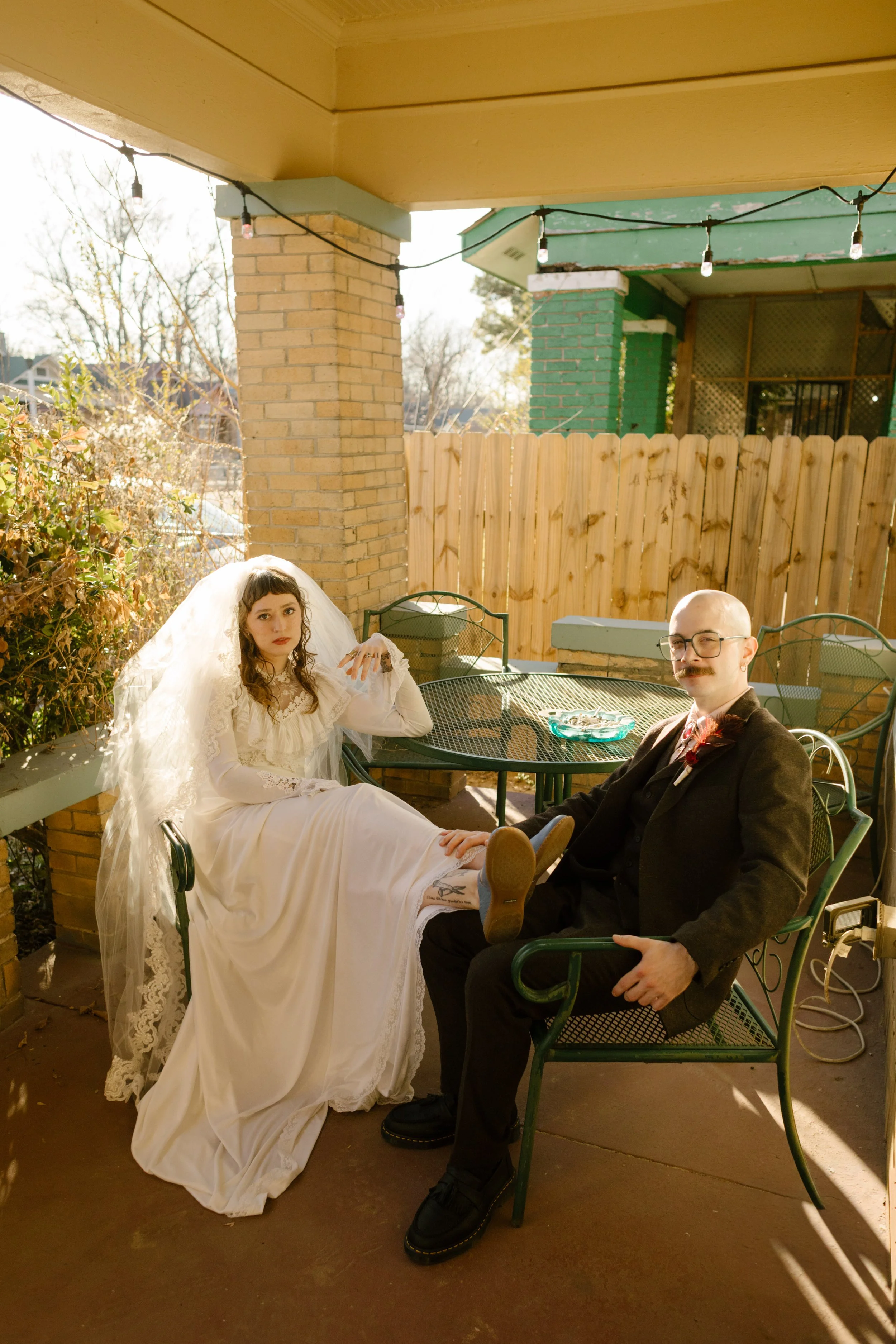 Bride and groom sitting on a sunlit porch in vintage-inspired attire, capturing relaxed and personality-filled unique wedding ideas