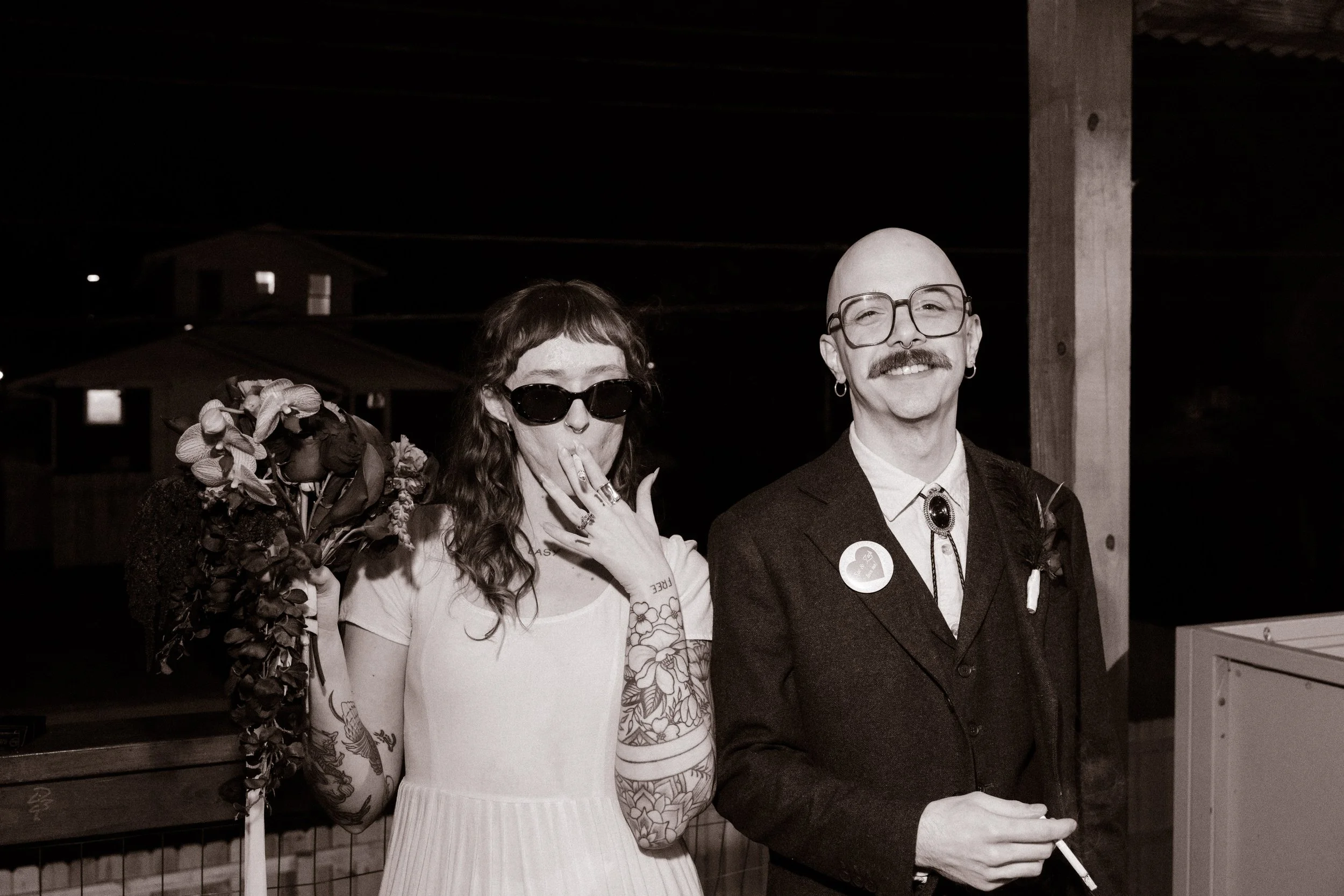 Bride and groom smoking together on porch at night with candid expressions, showcasing bold and unconventional unique wedding ideas