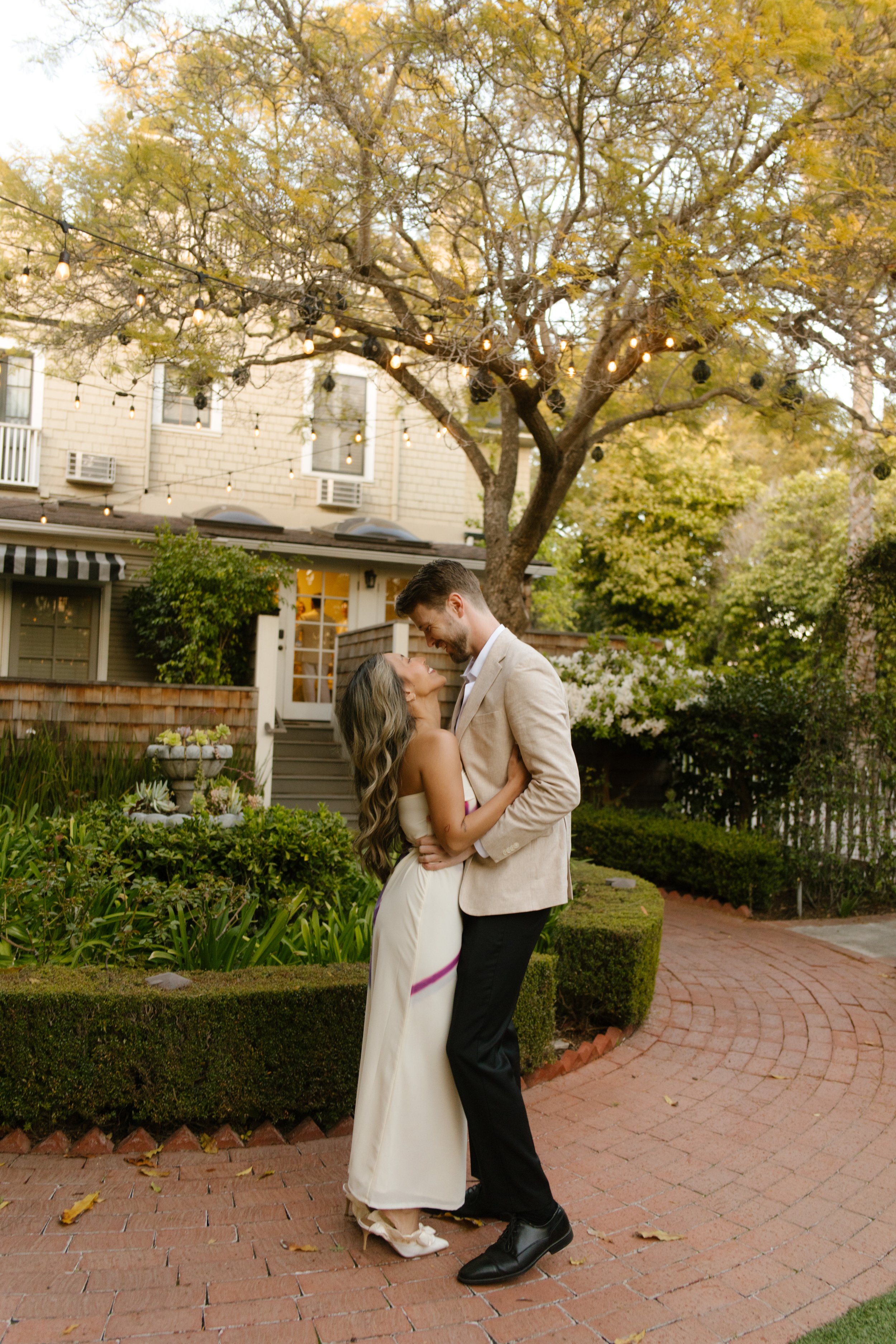 Couple embracing on a brick pathway under string lights in a garden during a wedding in Santa Barbara