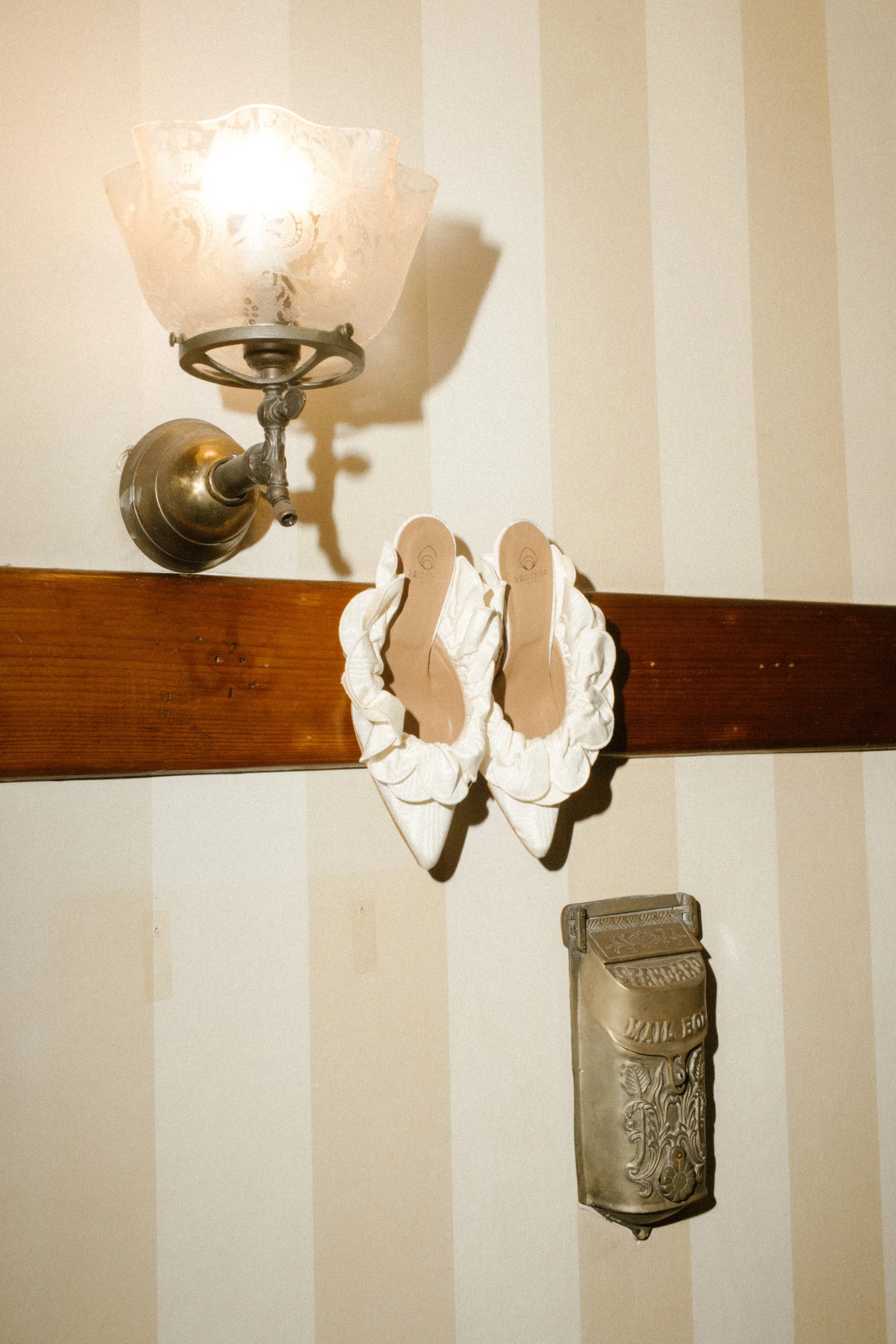 Bride’s shoes hanging on a vintage wall fixture with warm light and soft textures during a wedding in Santa Barbara