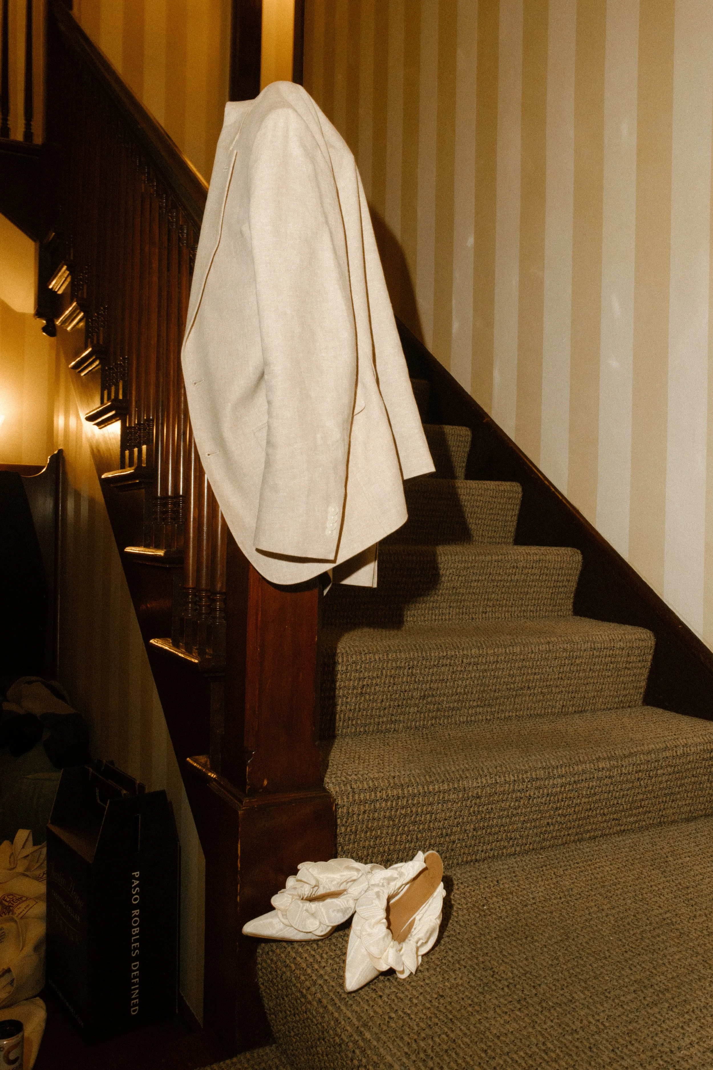 Groom’s jacket and bride’s shoes styled on a staircase with warm, editorial lighting