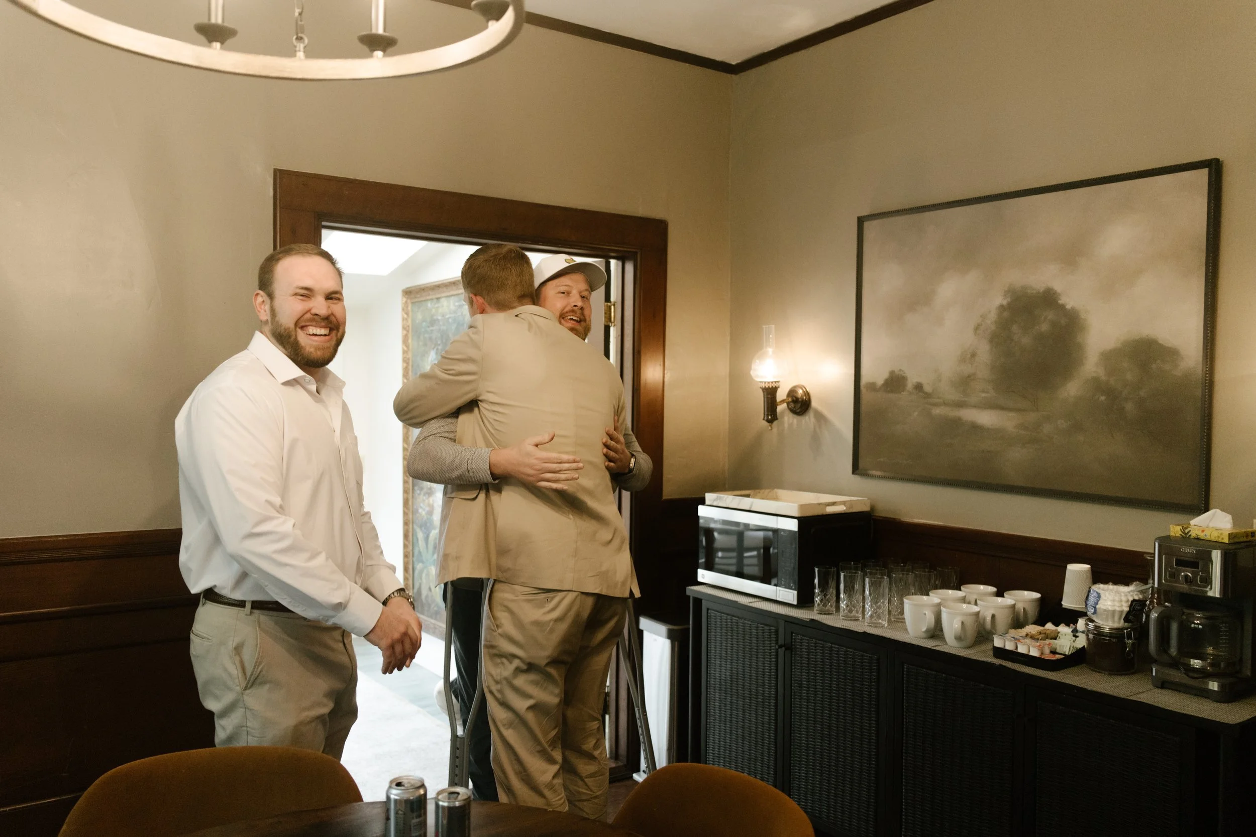 Groom hugging friends in a warm, candid moment indoors before the celebration begins