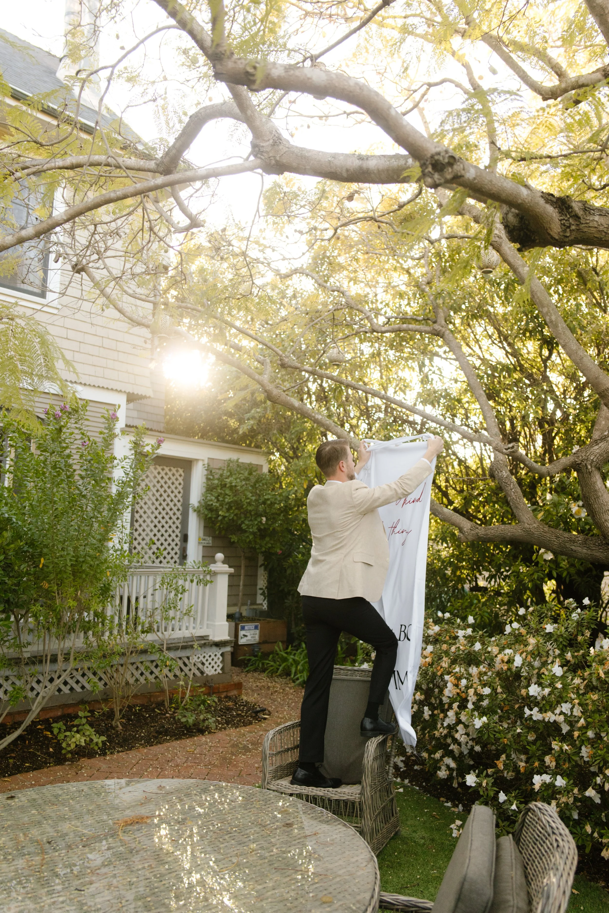 Groom standing on a chair hanging fabric in a garden setting during a wedding in Santa Barbara