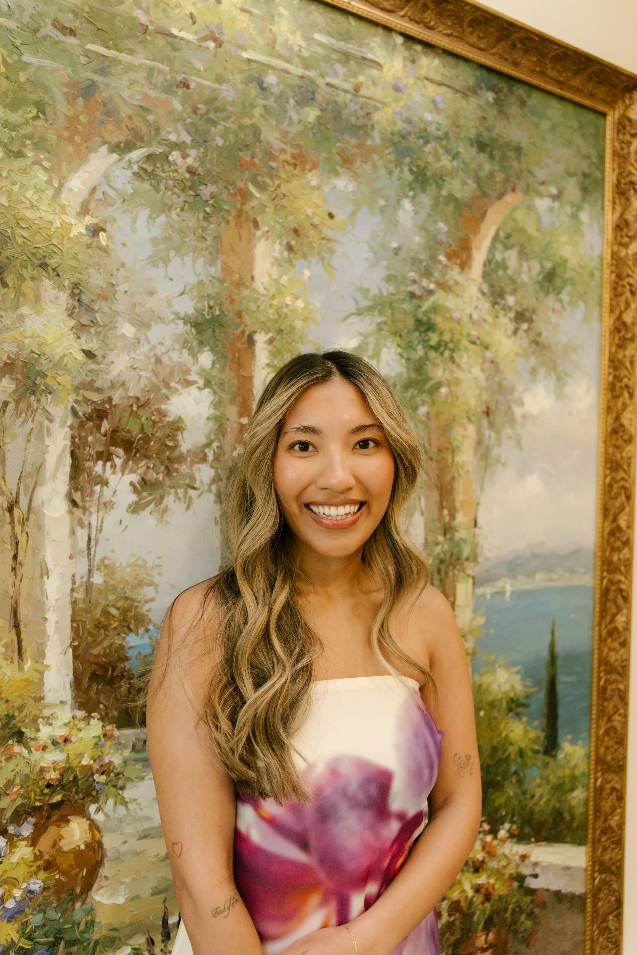 Portrait of a bride smiling in front of a romantic landscape painting indoors