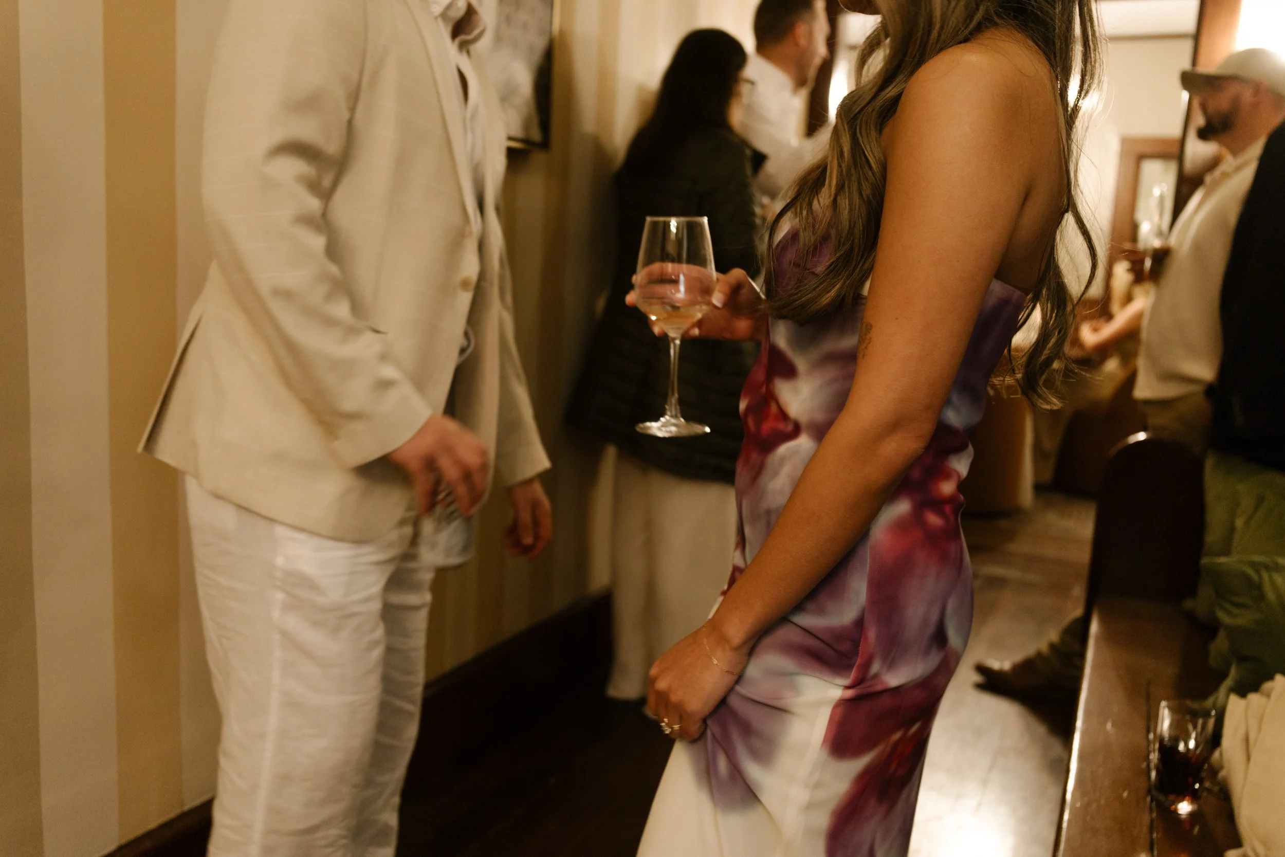 Candid moment of guests standing and talking indoors with drinks in hand during a wedding celebration