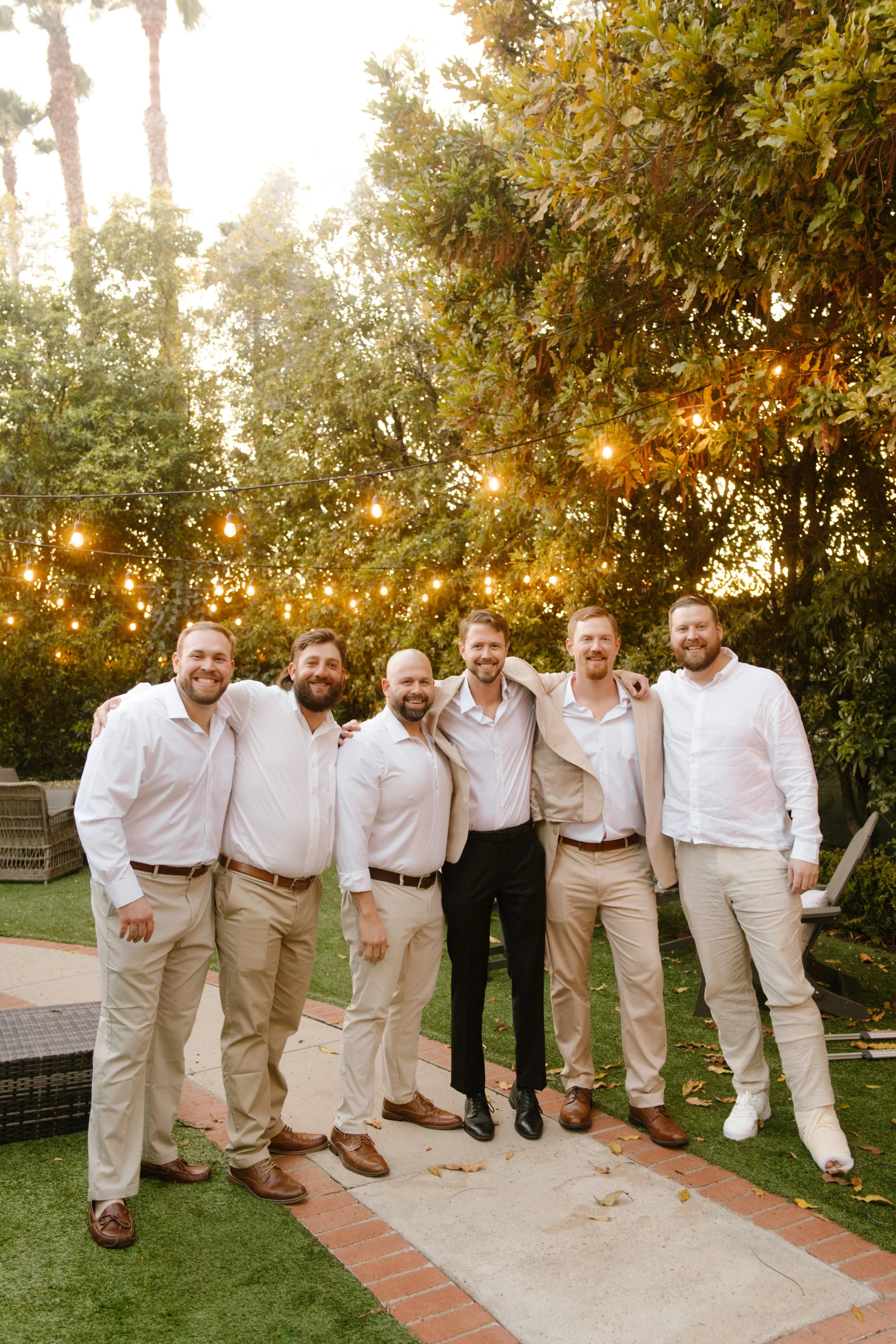 Group of groomsmen standing together outdoors under string lights during a wedding in Santa Barbara