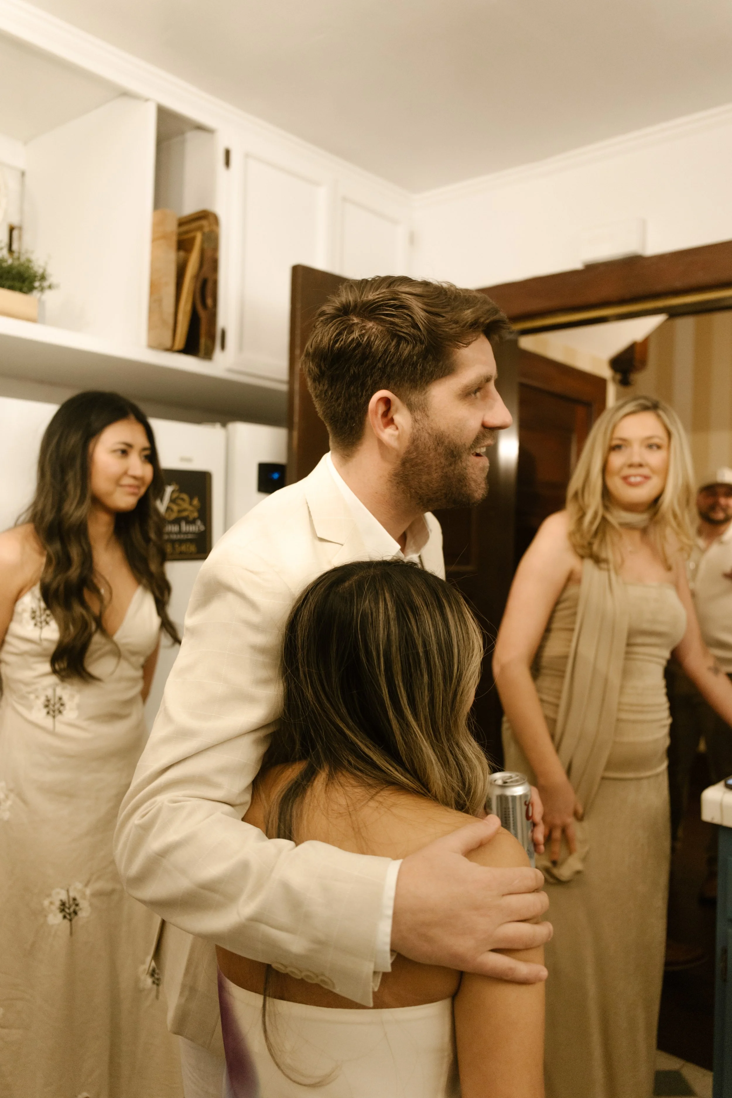 Couple embracing in a kitchen surrounded by friends during a candid wedding moment