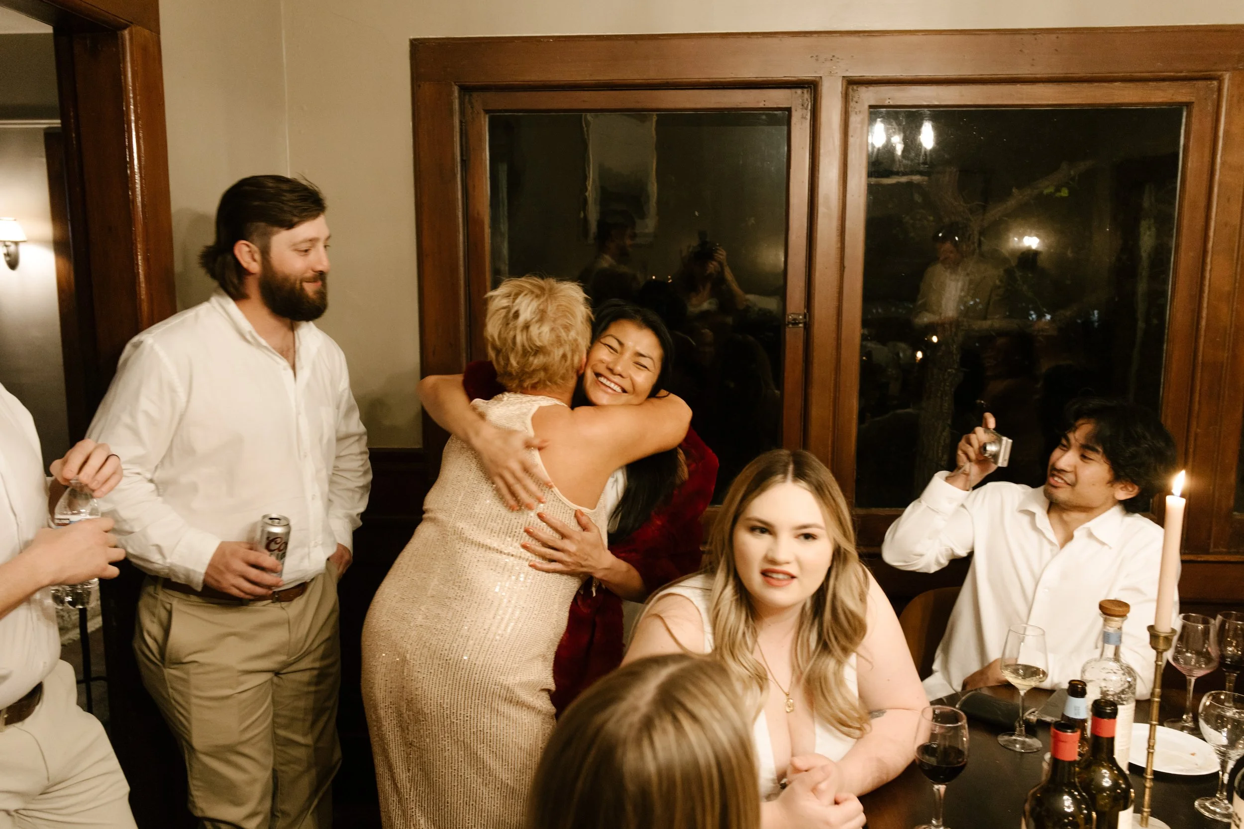 Friends embracing and celebrating together around a dining table during a wedding in Santa Barbara