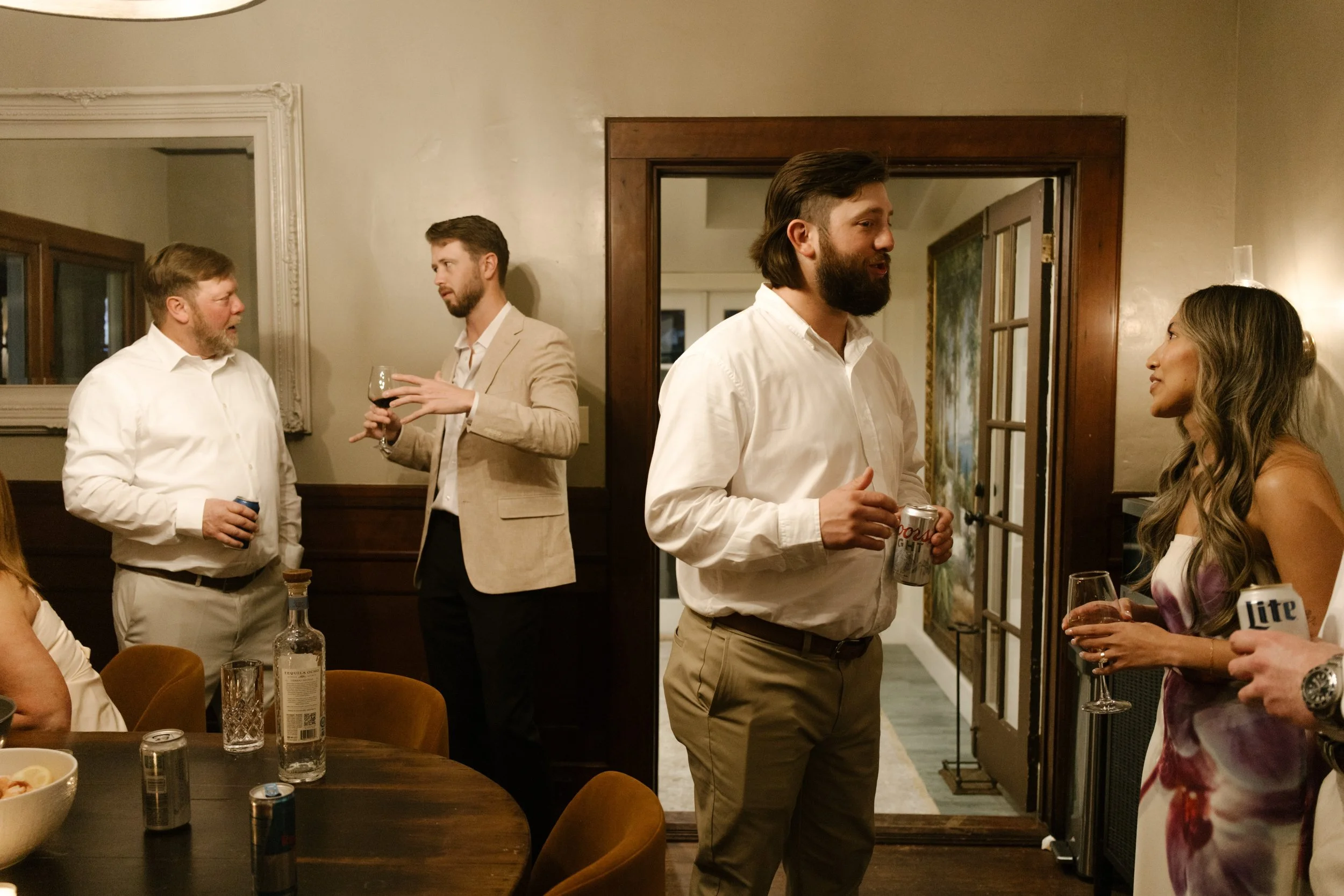 Guests talking and holding drinks in a warmly lit interior space during a candid wedding moment
