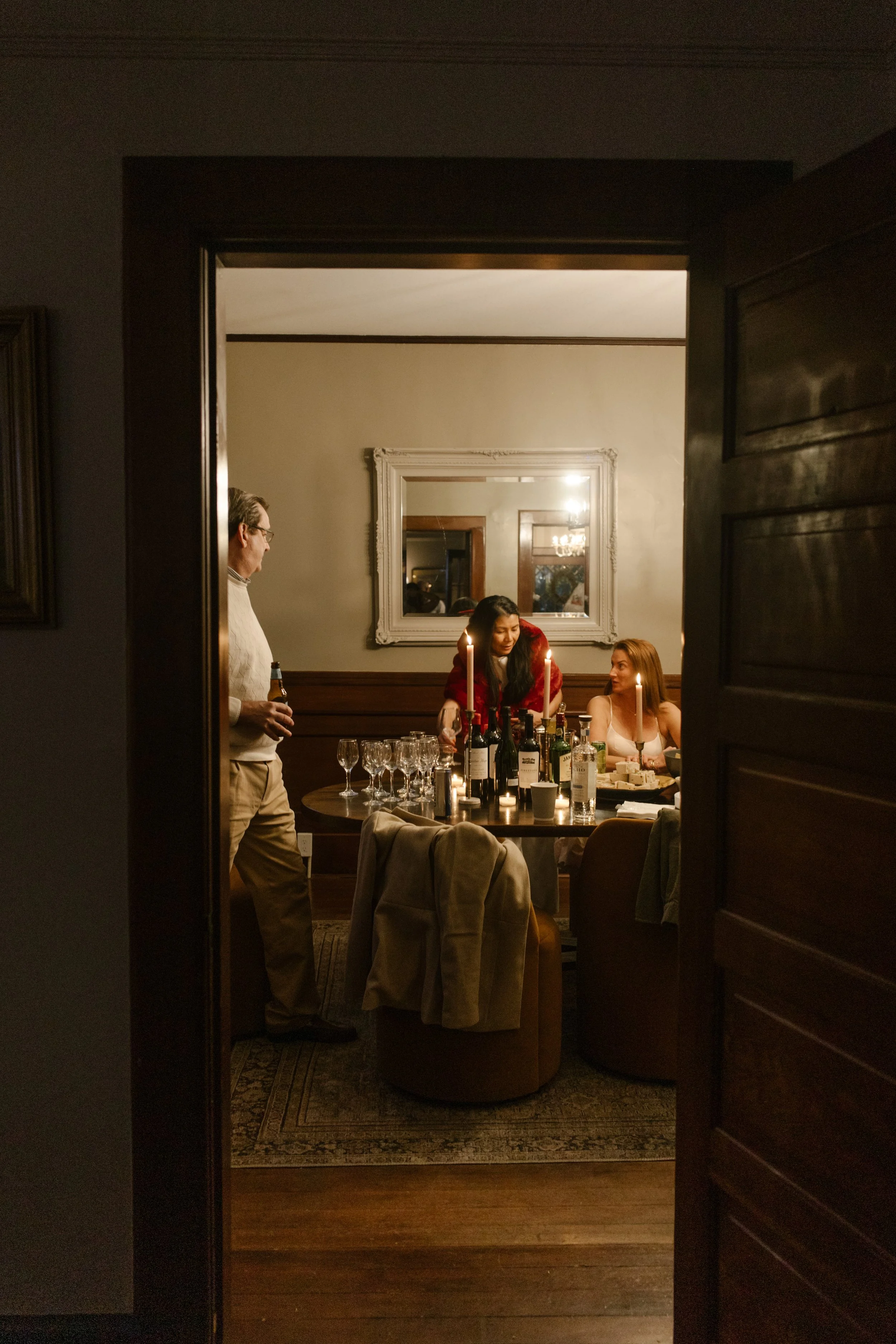 View through a doorway into a candlelit dinner scene with guests gathered around the table
