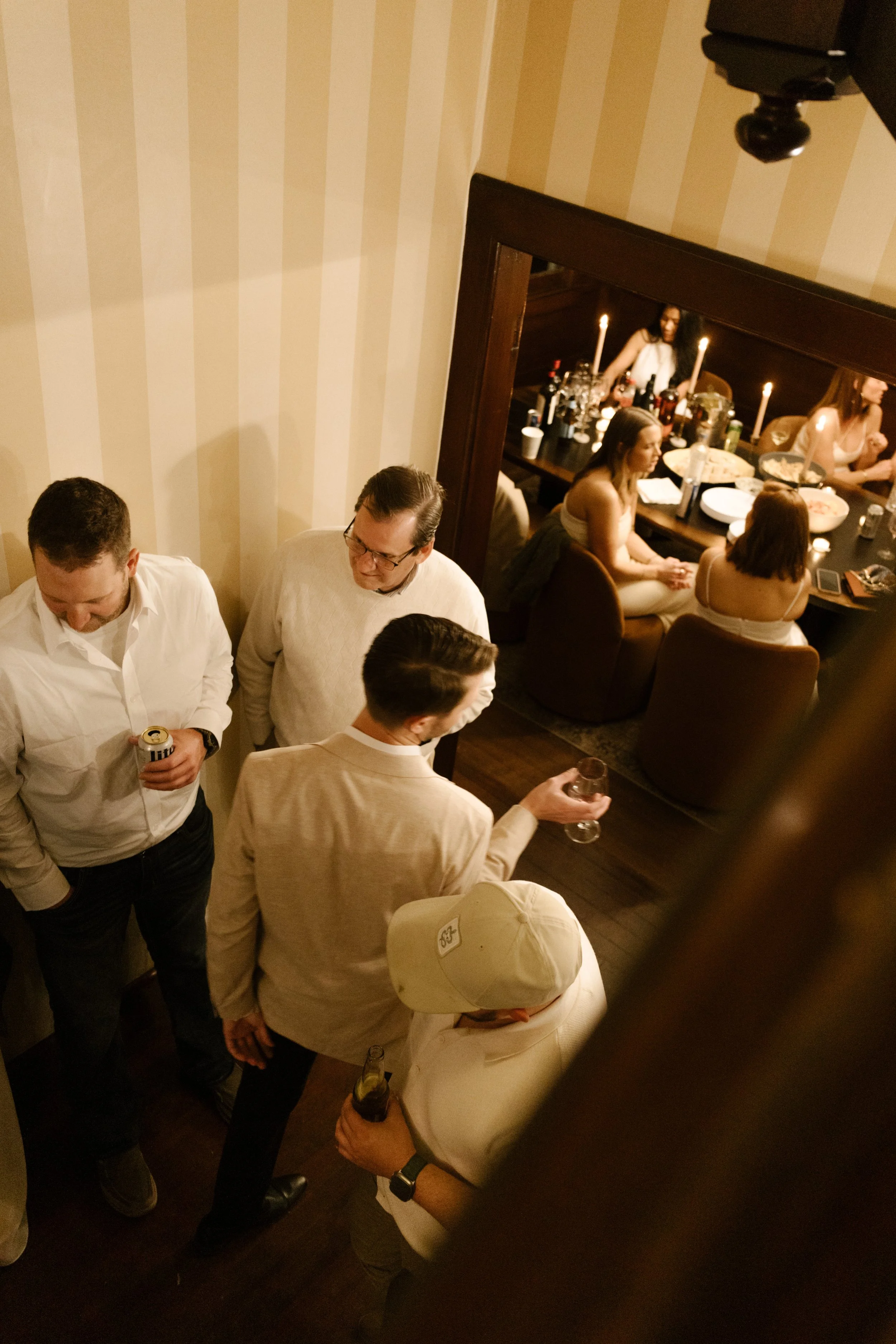 Overhead view of guests gathered in a hallway with drinks while dinner continues in the next room during a wedding in Santa Barbara