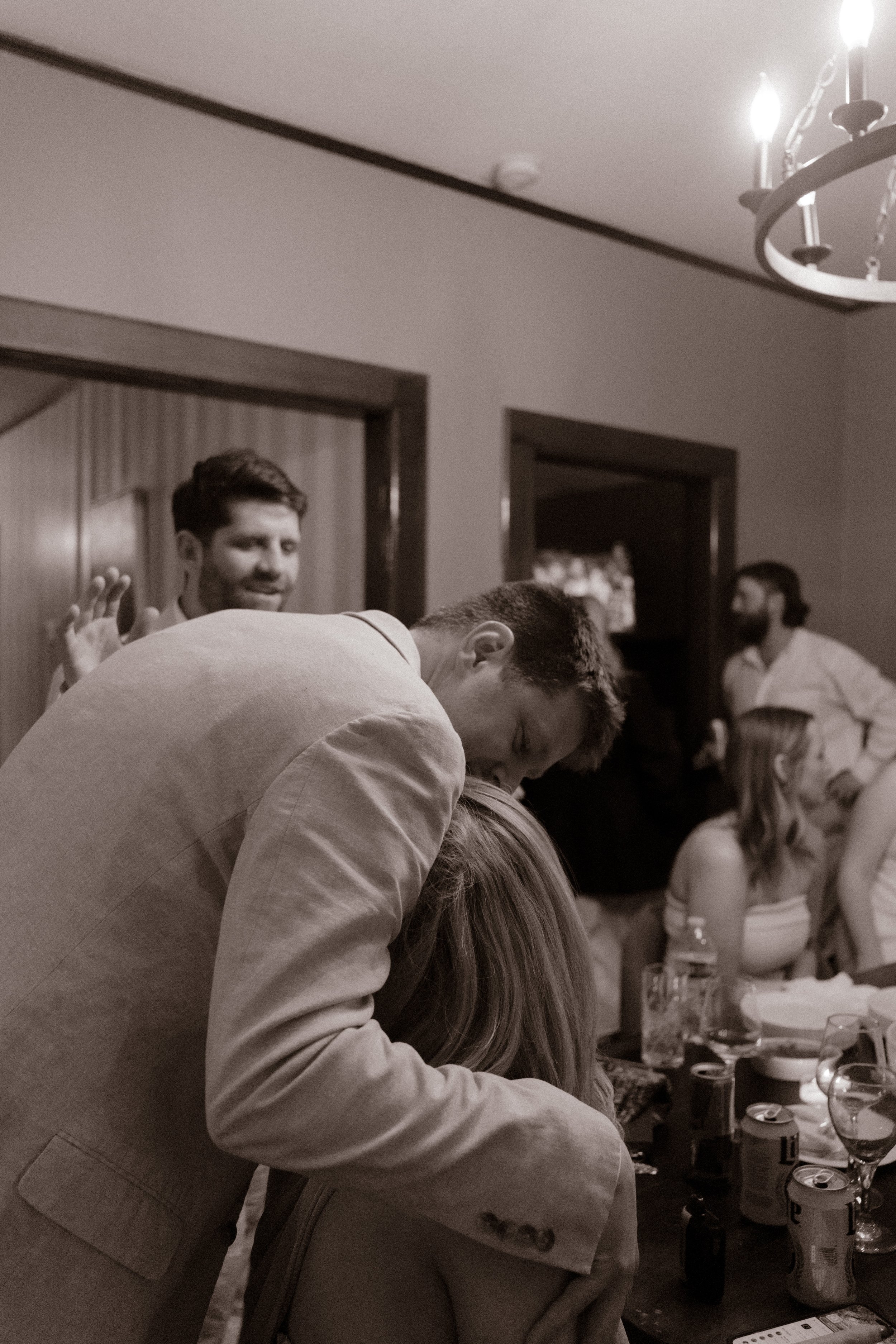 Black and white candid of couple embracing in a crowded room during an emotional moment at a wedding