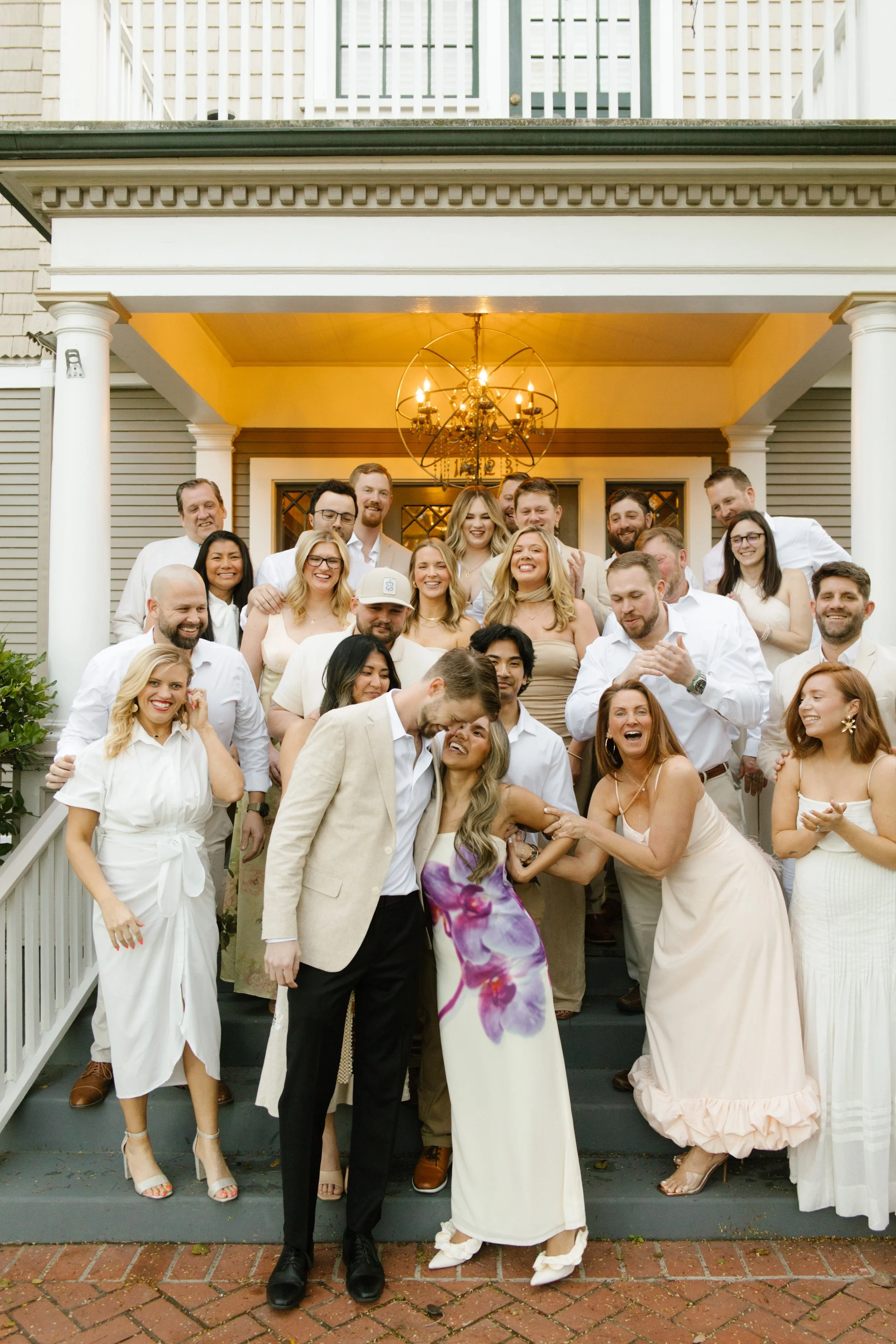 Large group of wedding guests gathered on front steps for a celebratory group photo