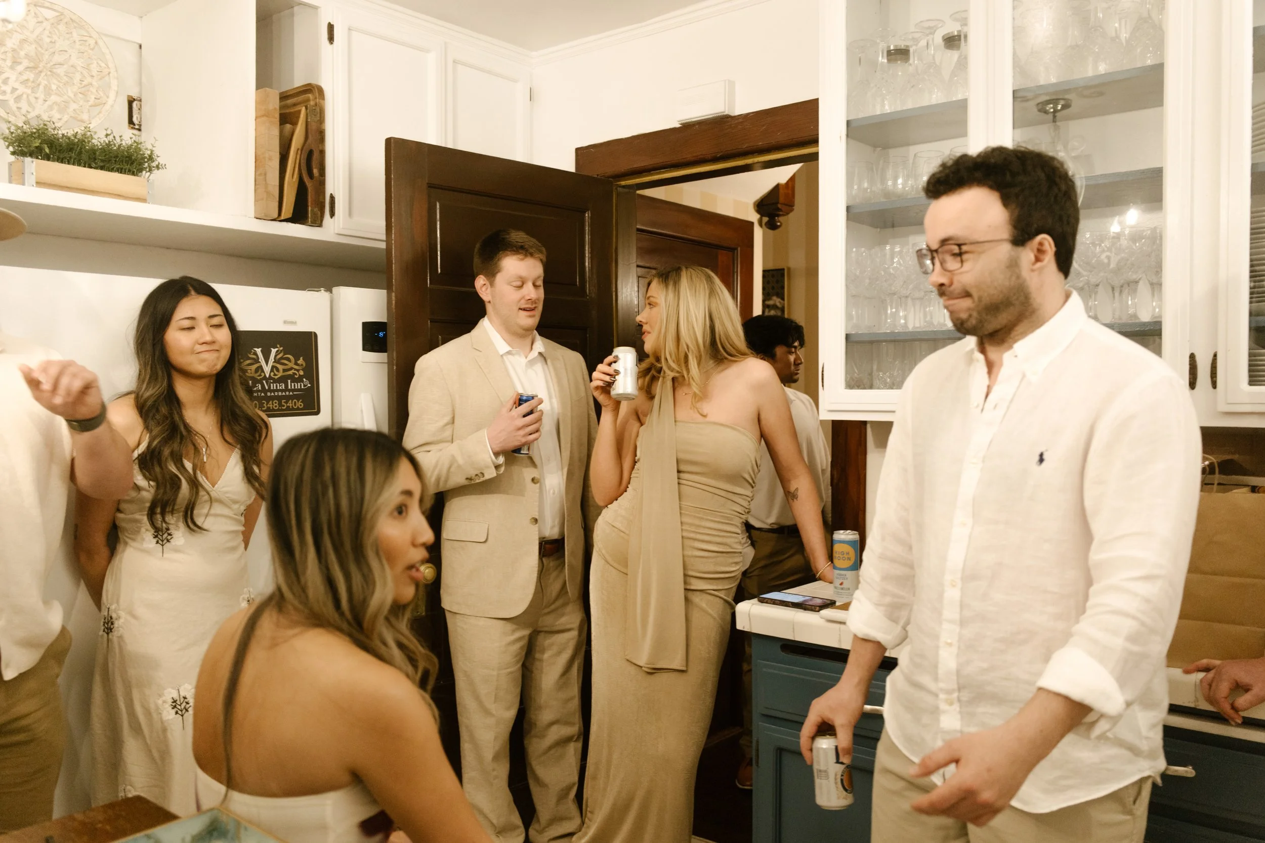Friends gathered in a kitchen sharing drinks and conversation during a relaxed wedding celebration