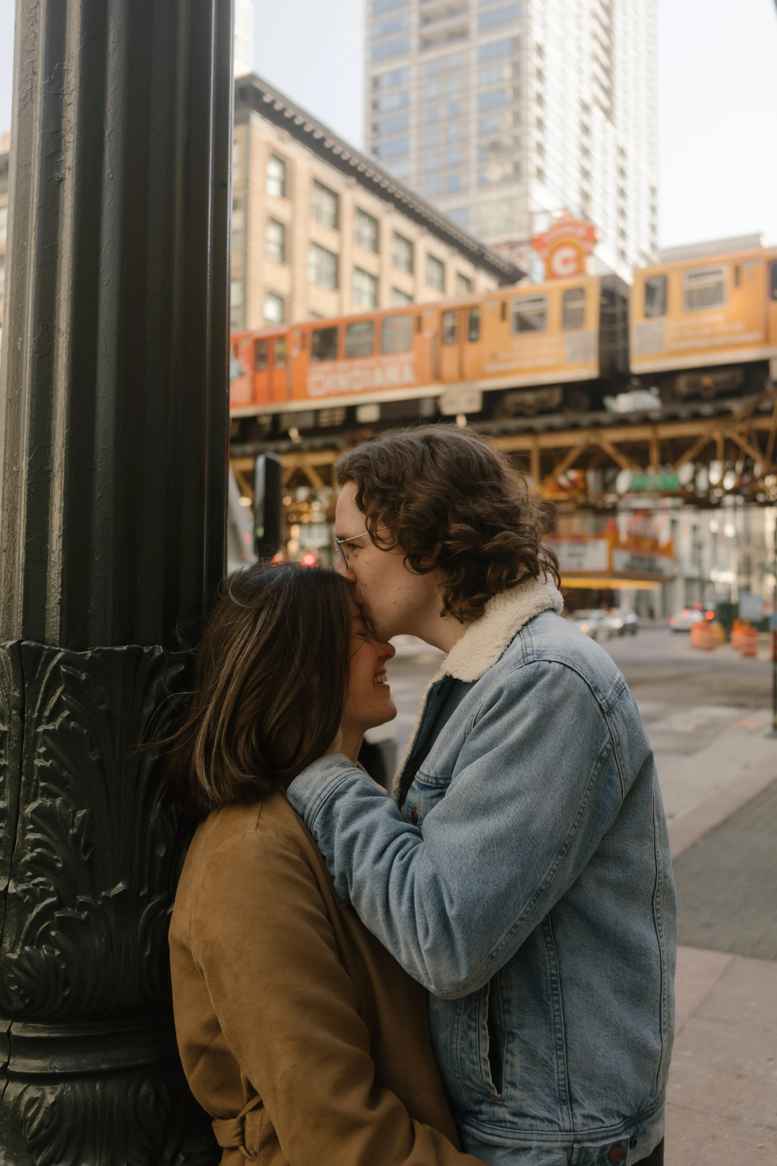 Close-up of couple sharing a quiet moment near a city streetlight as a train passes overhead in downtown Chicago during engagement photos in Chicago