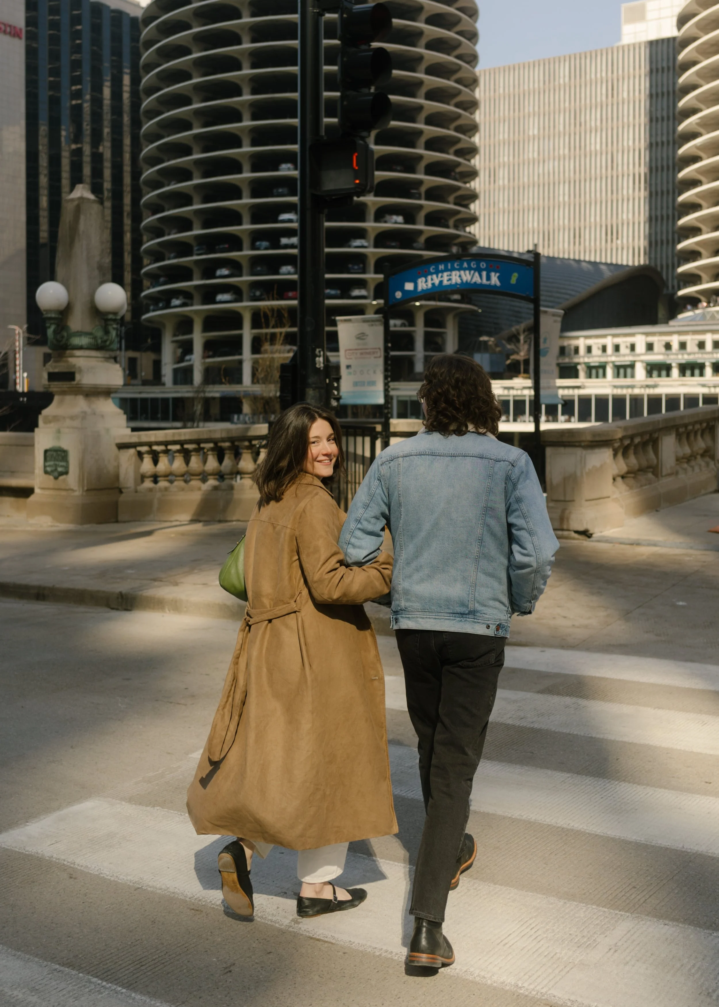 Couple walking across a crosswalk near Marina City towers with one partner glancing back and smiling during engagement photos in Chicago