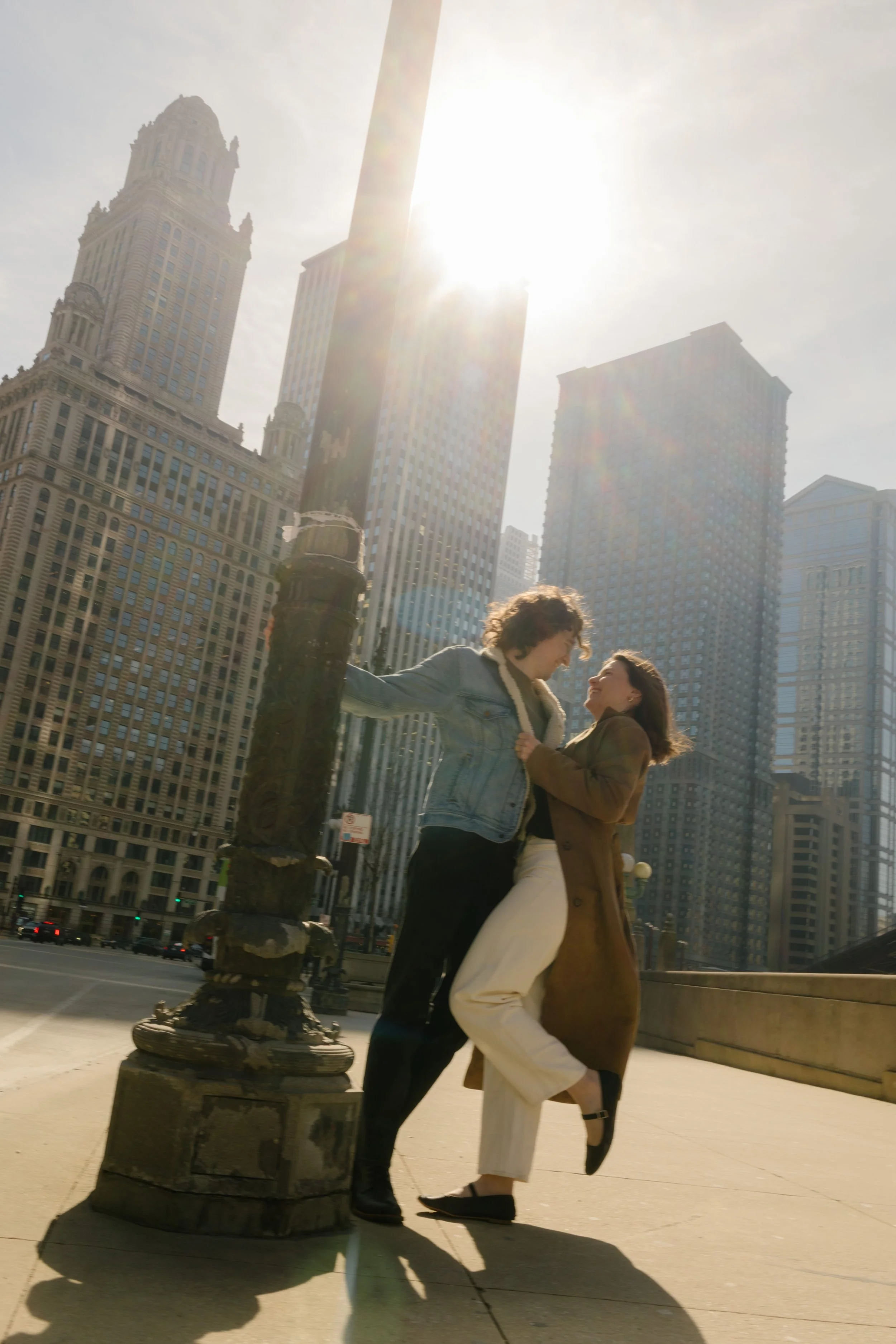Couple laughing together beside a vintage streetlight on a Chicago bridge with bright city light and tall buildings surrounding them