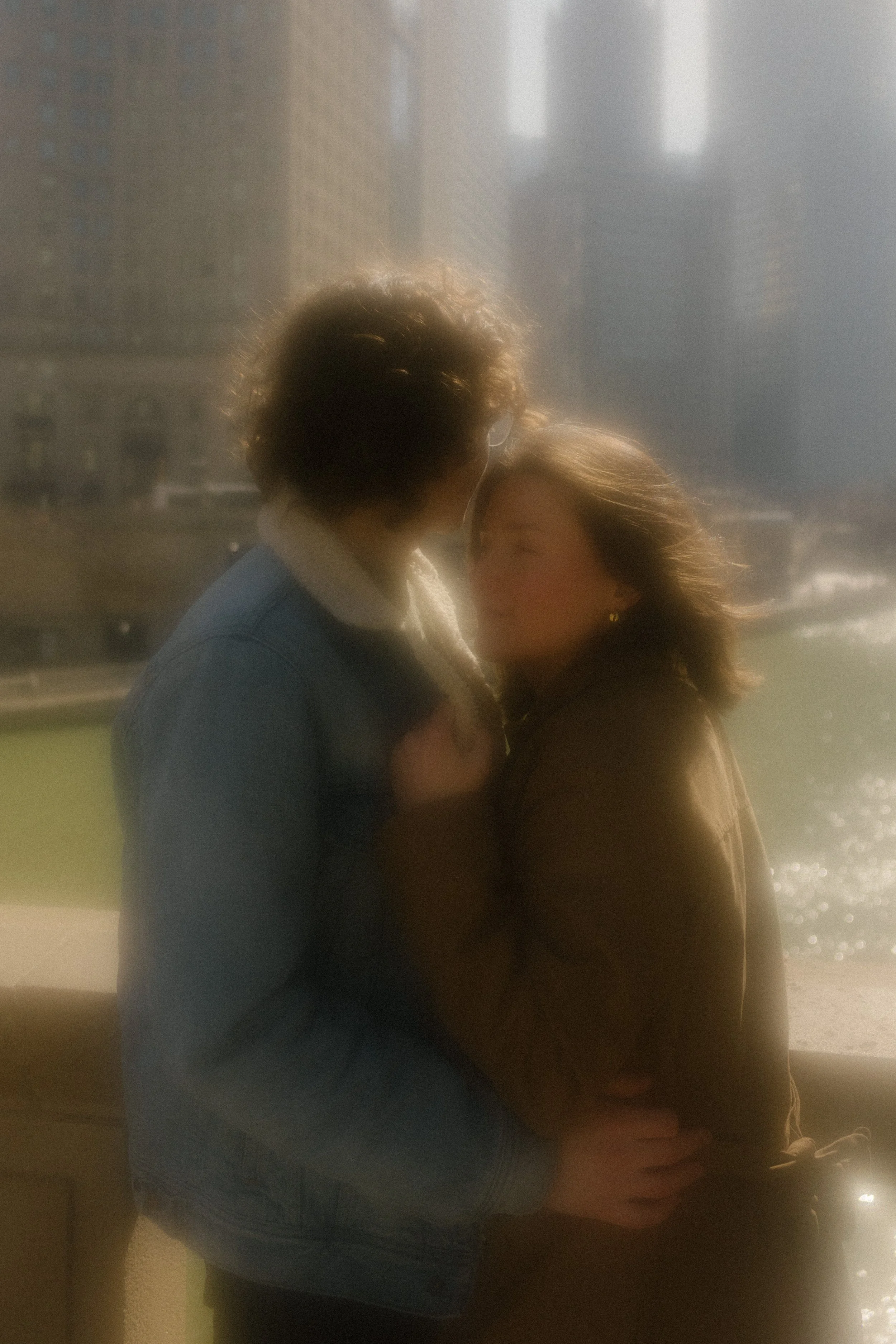 Glowy close-up of couple embracing with soft sunlight and blurred Chicago skyline behind them