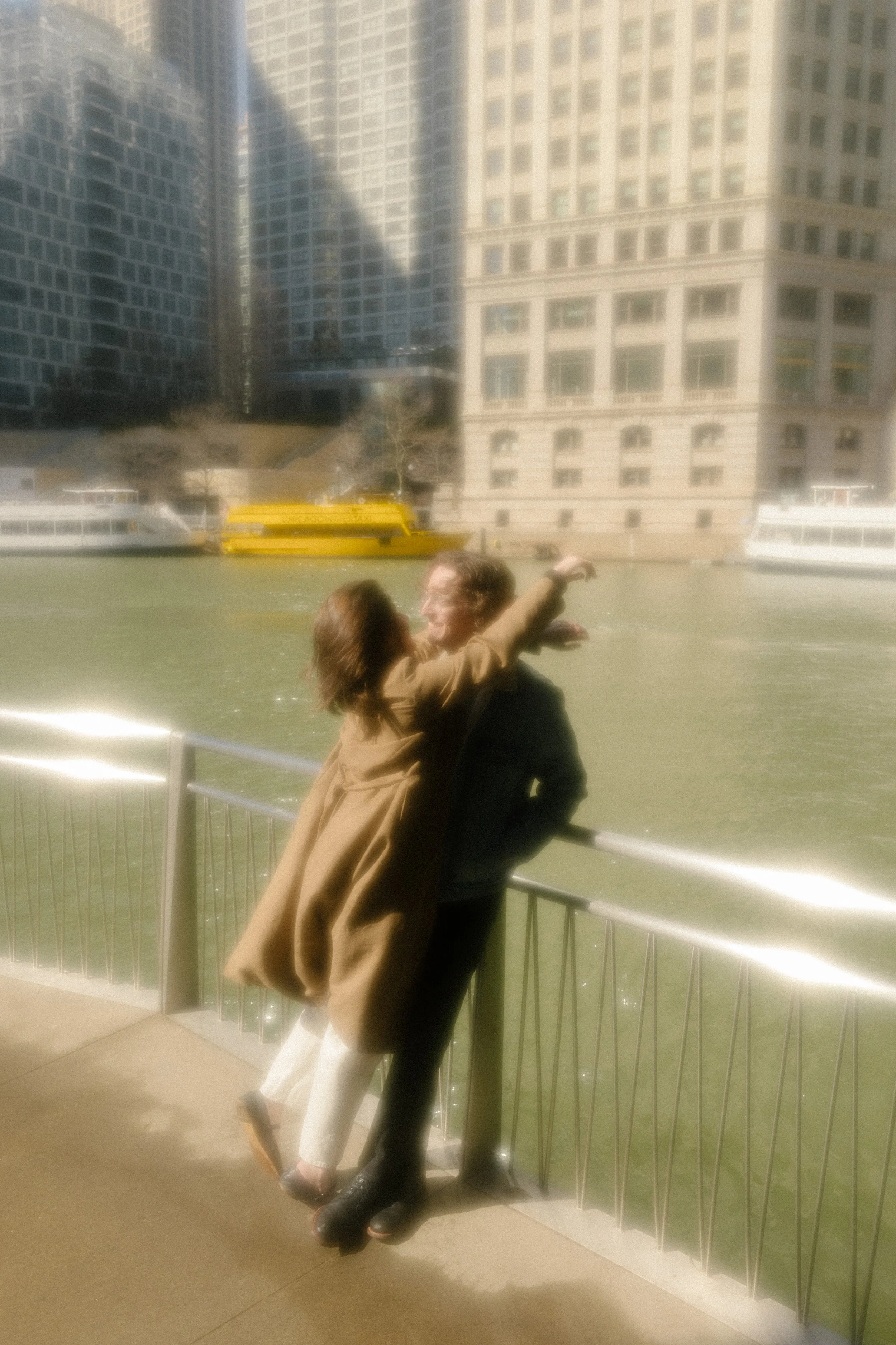 Dreamy, soft-focus moment of couple laughing and leaning into each other along the riverwalk railing during engagement photos in Chicago