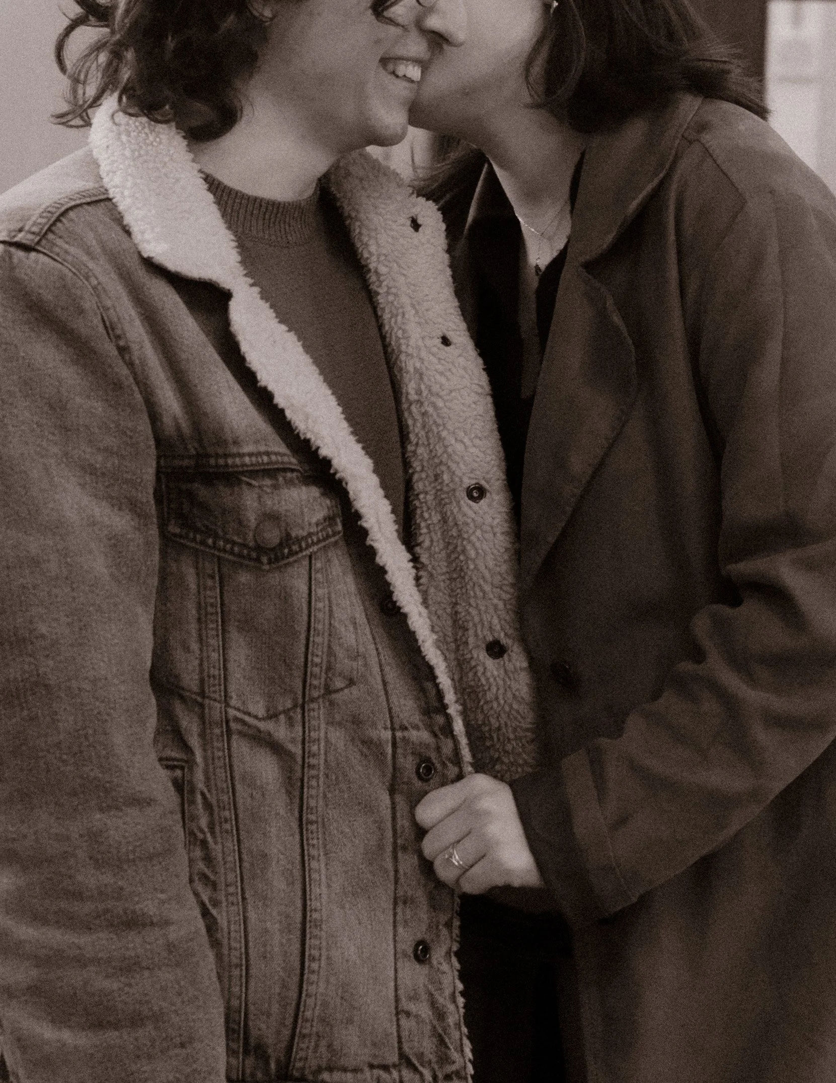 Black and white close-up of couple smiling as one leans in for a kiss, capturing a quiet moment during engagement photos in Chicago