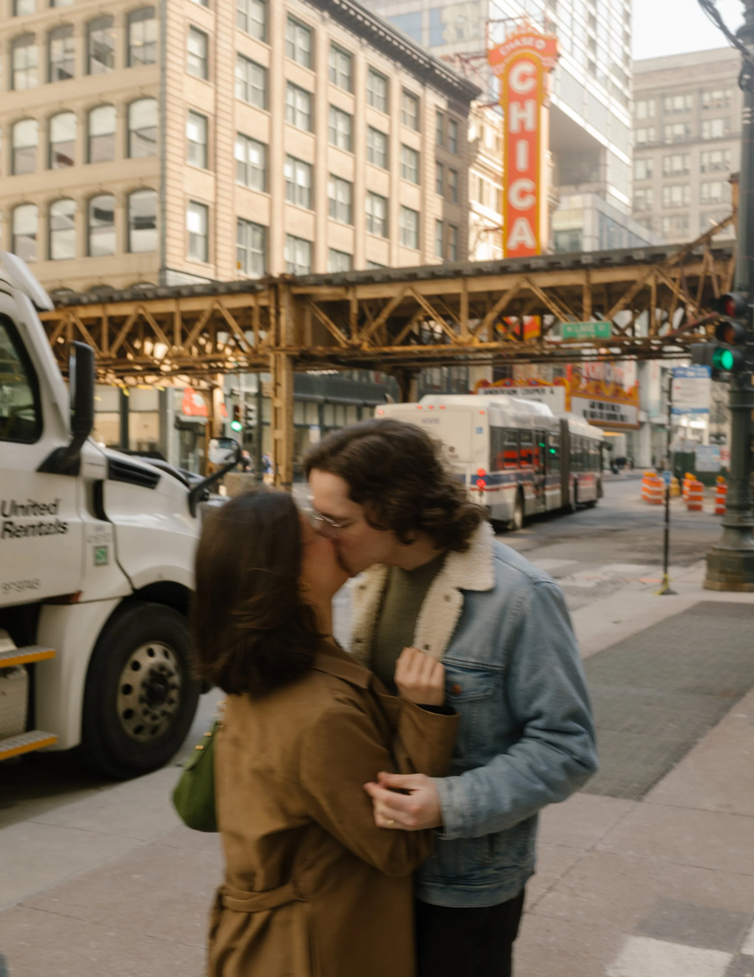 Couple kissing on a downtown Chicago street beneath the elevated train tracks with the Chicago Theatre sign in the background