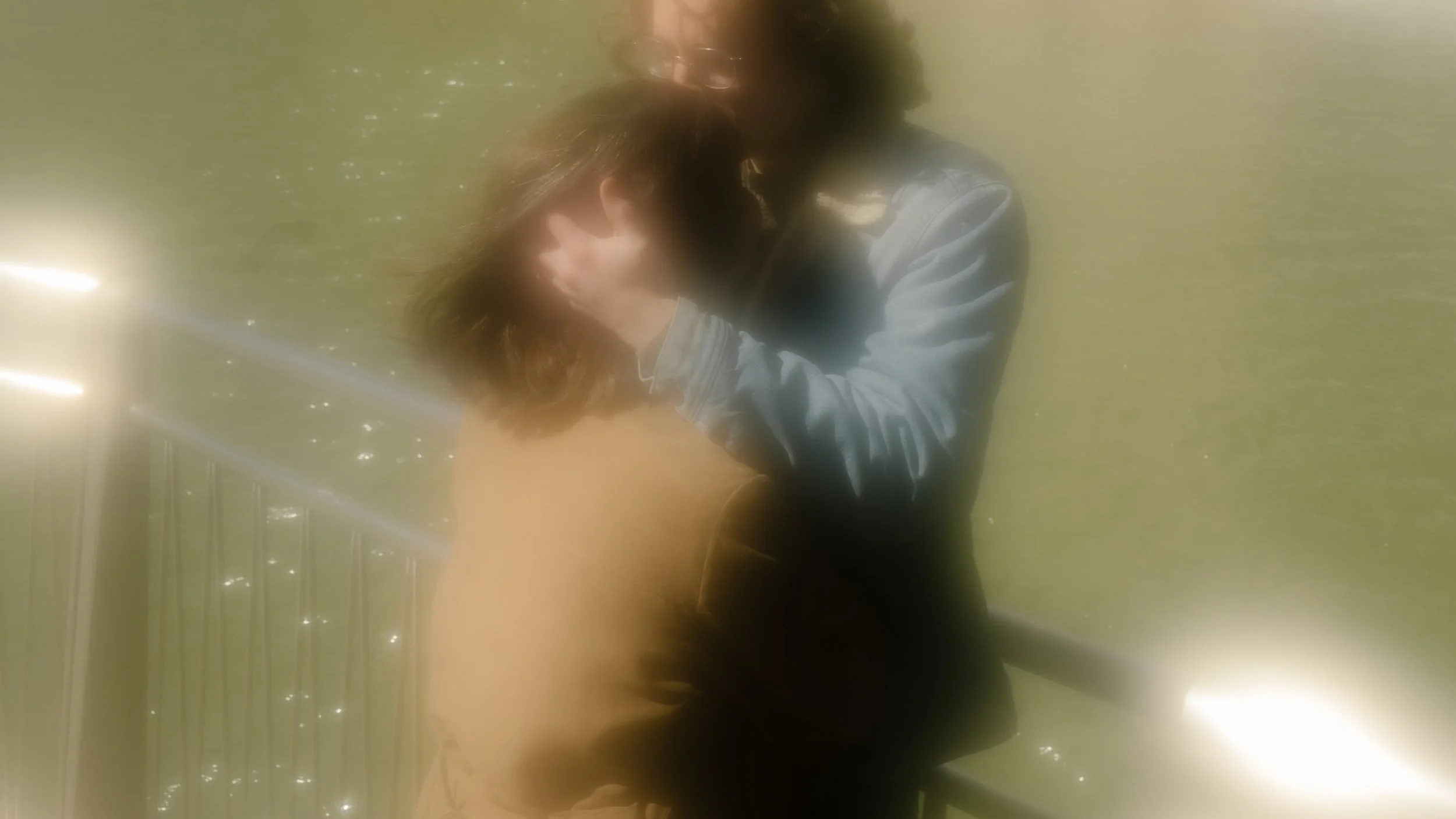 Soft, blurred close-up of couple hugging with sunlight reflecting off the river behind them