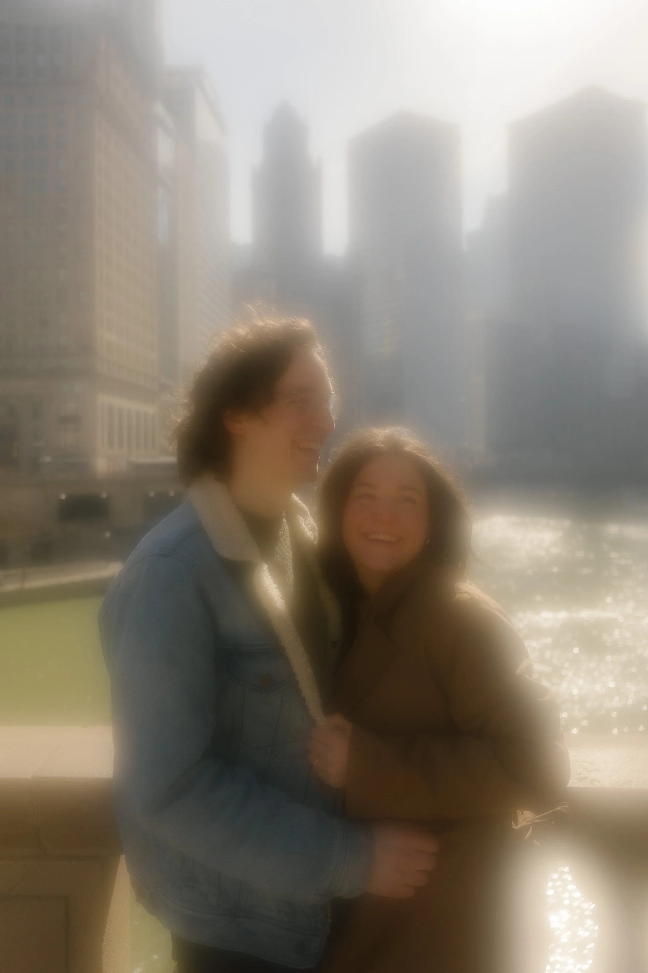 Glowy, backlit portrait of couple standing close and smiling with the Chicago skyline behind them during engagement photos in Chicago