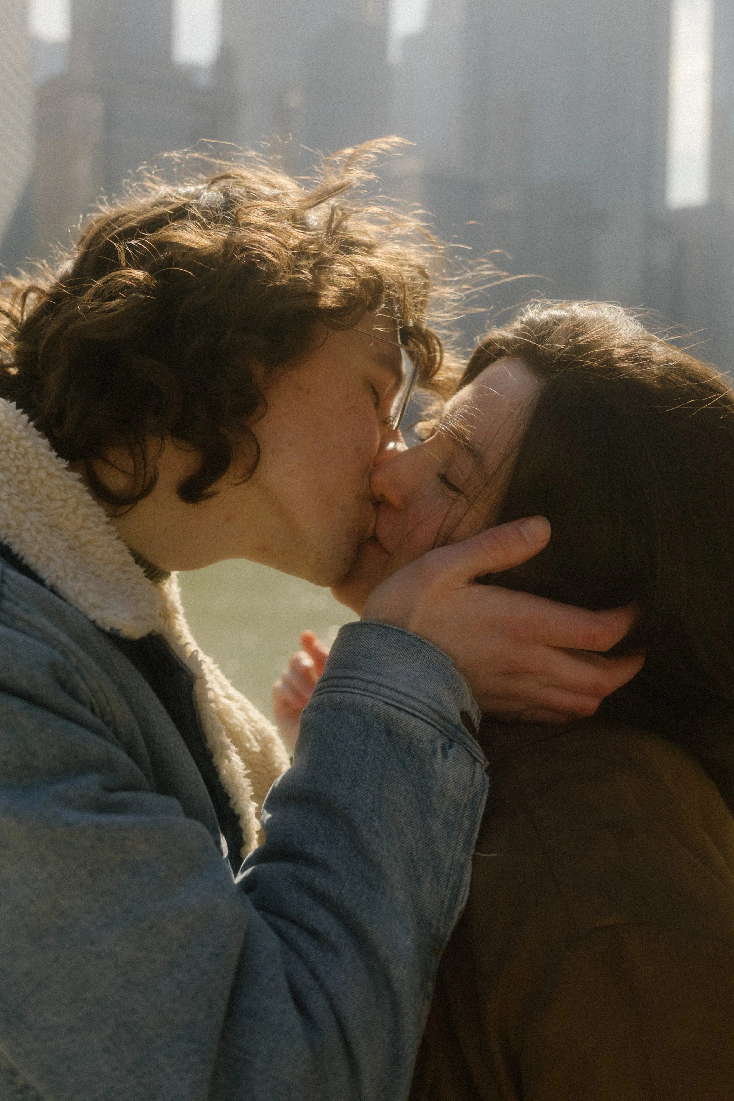 Close-up of couple kissing with soft sunlight and blurred city buildings behind them