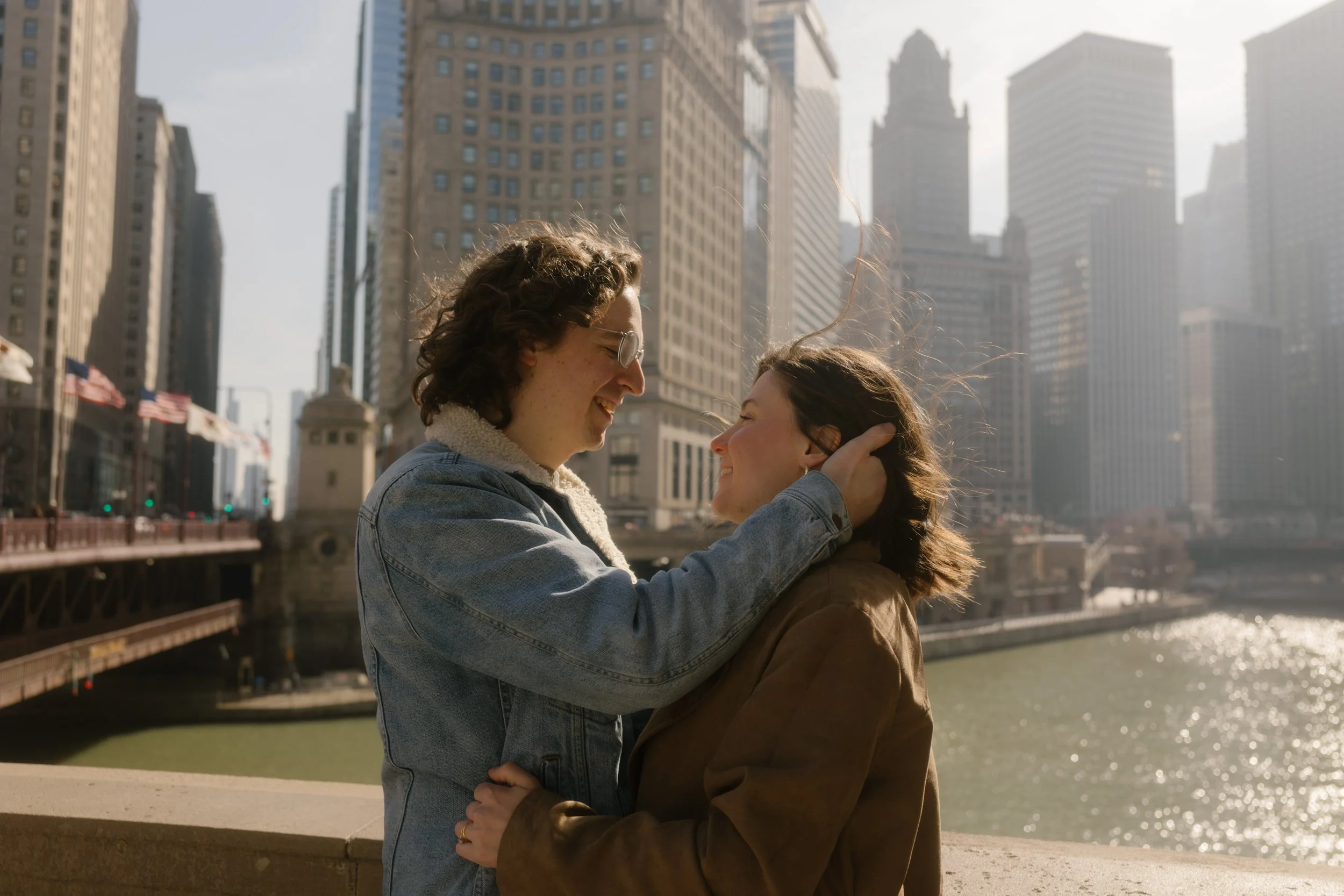 Couple standing close together along the riverwalk, smiling and leaning in with skyline views during engagement photos in Chicago