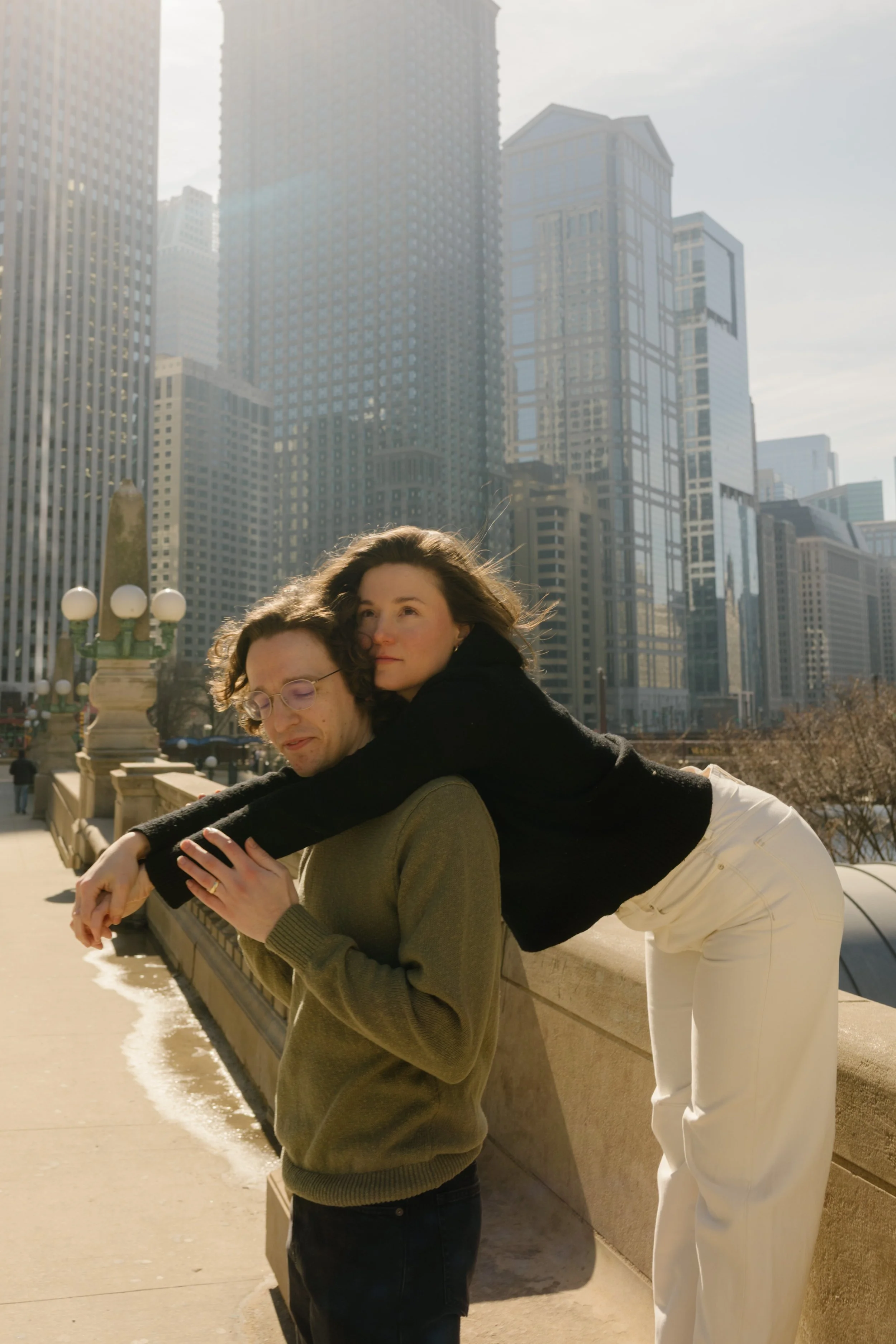 Playful moment with one partner leaning over the other along a stone bridge, surrounded by downtown Chicago architecture during engagement photos in Chicago