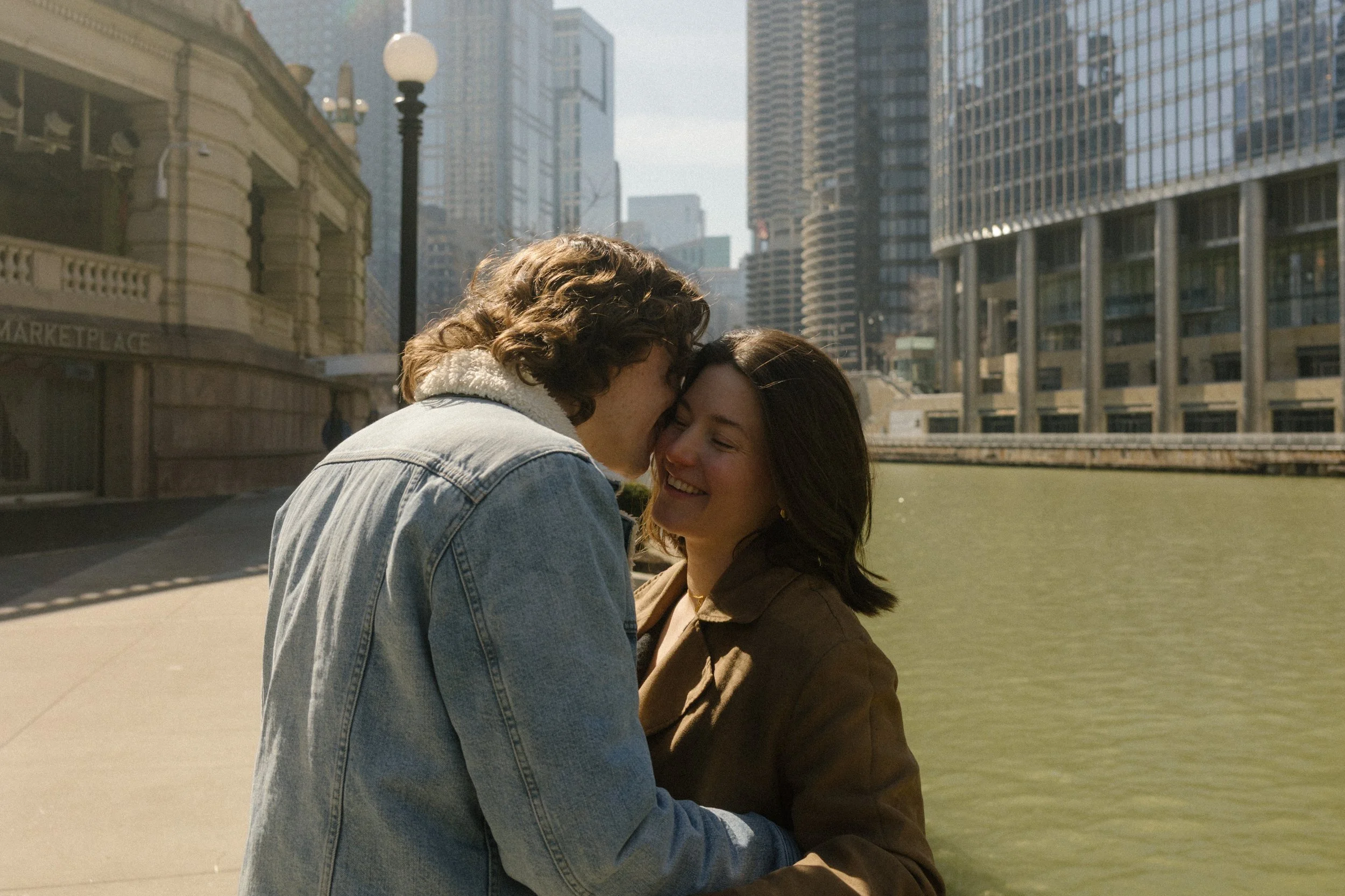 Close-up of couple smiling and leaning into each other along the Chicago River with skyline views during engagement photos in Chicago
