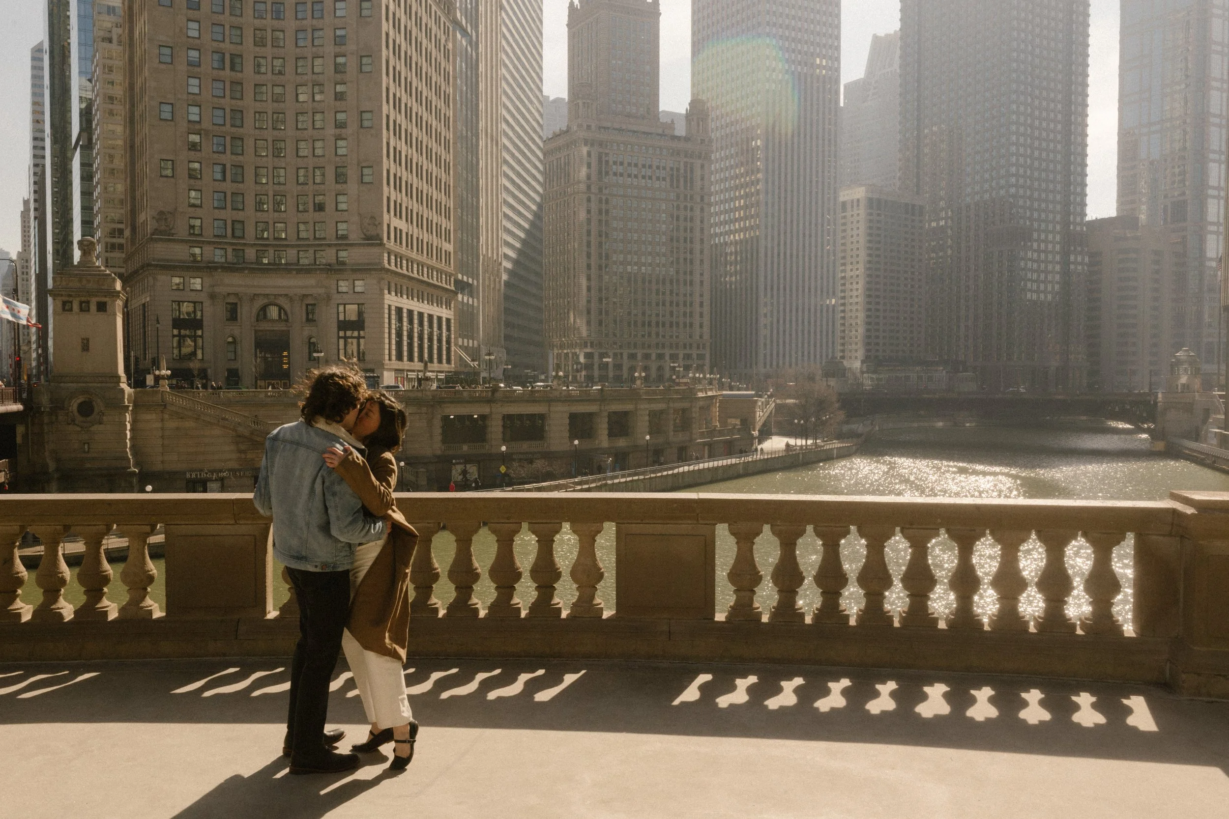 Couple hugging along the Chicago River with skyline views and soft golden light during engagement photos in Chicago